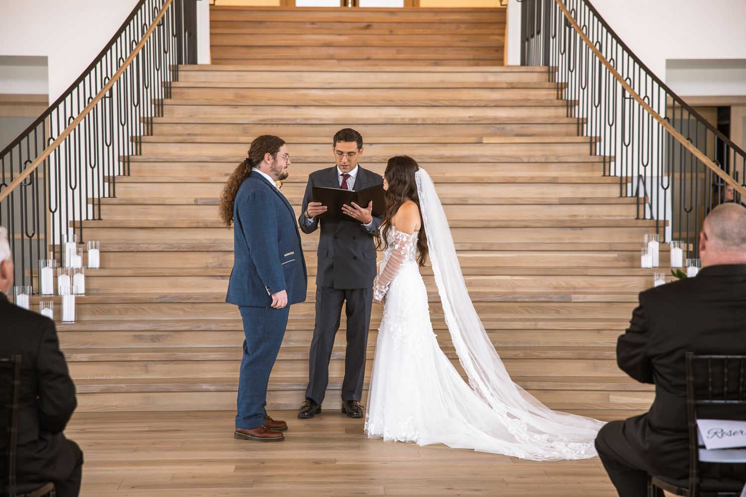 Wedding party poses on elegant wooden staircase in formal attire.