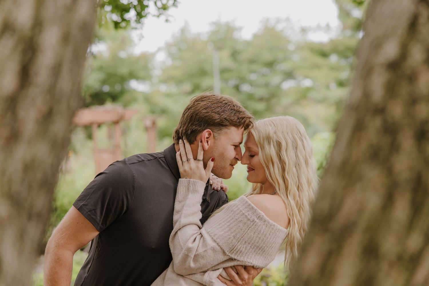 Romantic couple embracing in a wooded setting with soft natural lighting.