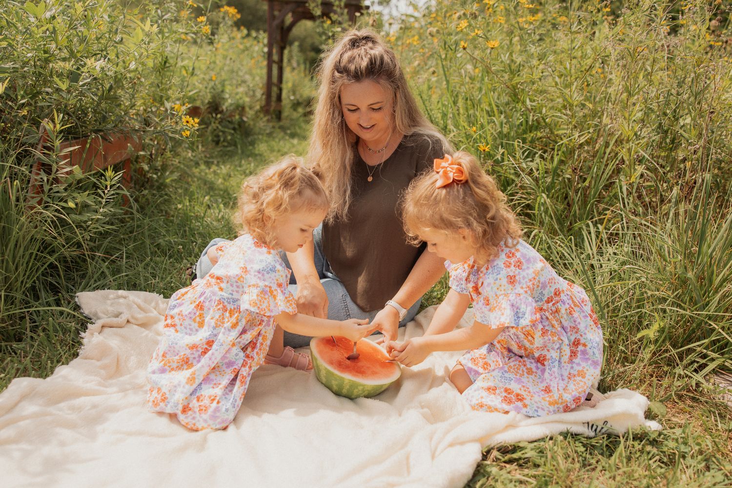 A summer picnic scene with matching floral dresses and fresh watermelon on a blanket.
