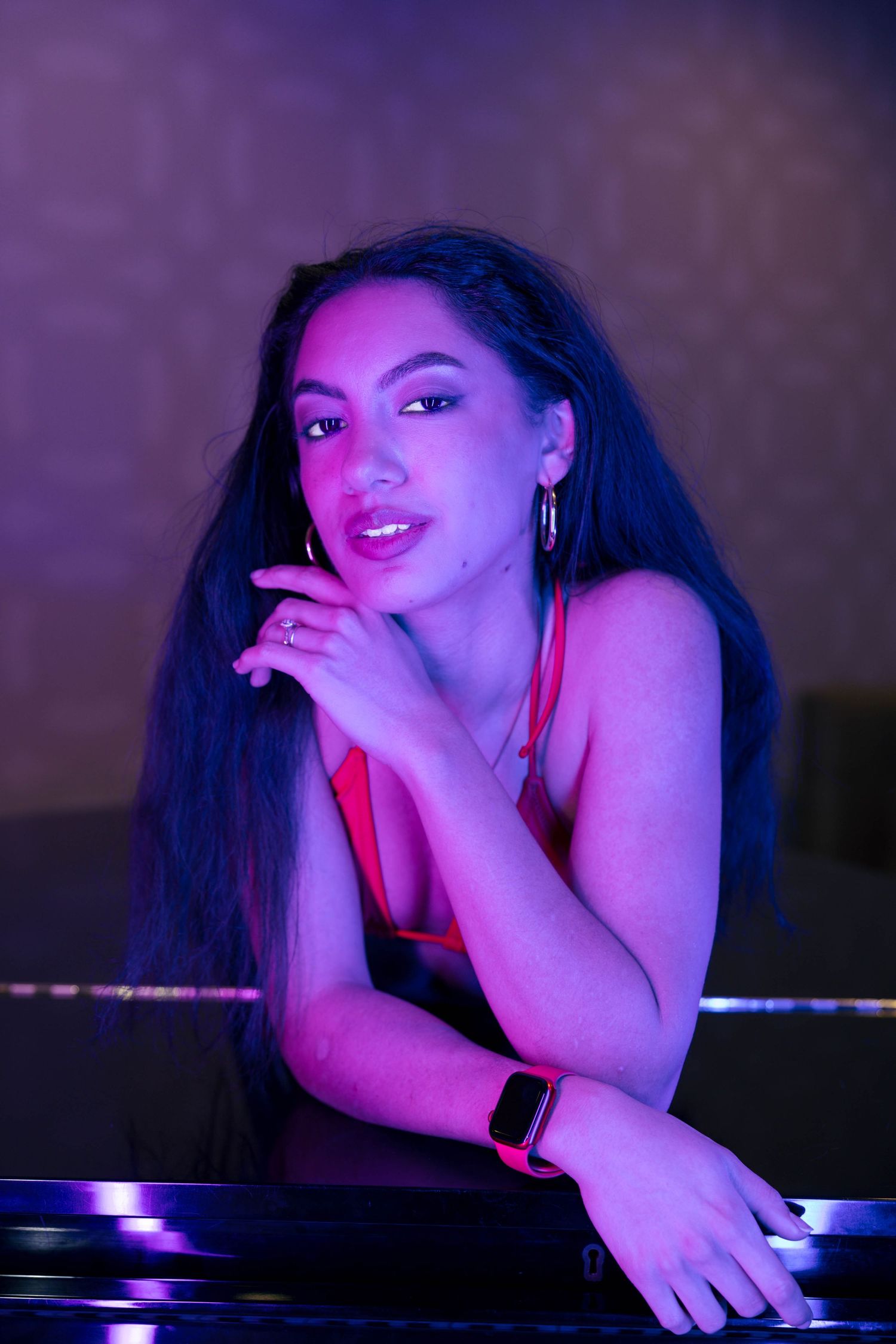 Young woman with long hair posing by a grand piano in atmospheric purple neon lighting.