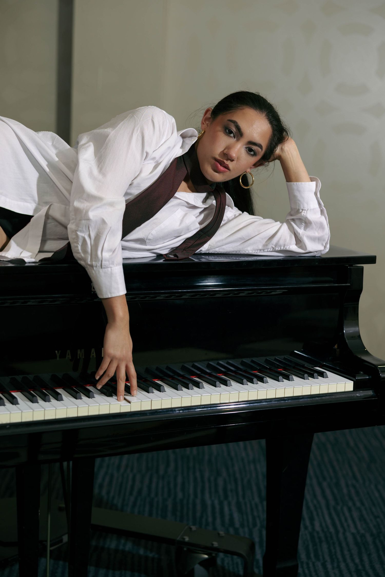 Young woman in white shirt leaning on grand piano keys in elegant room.