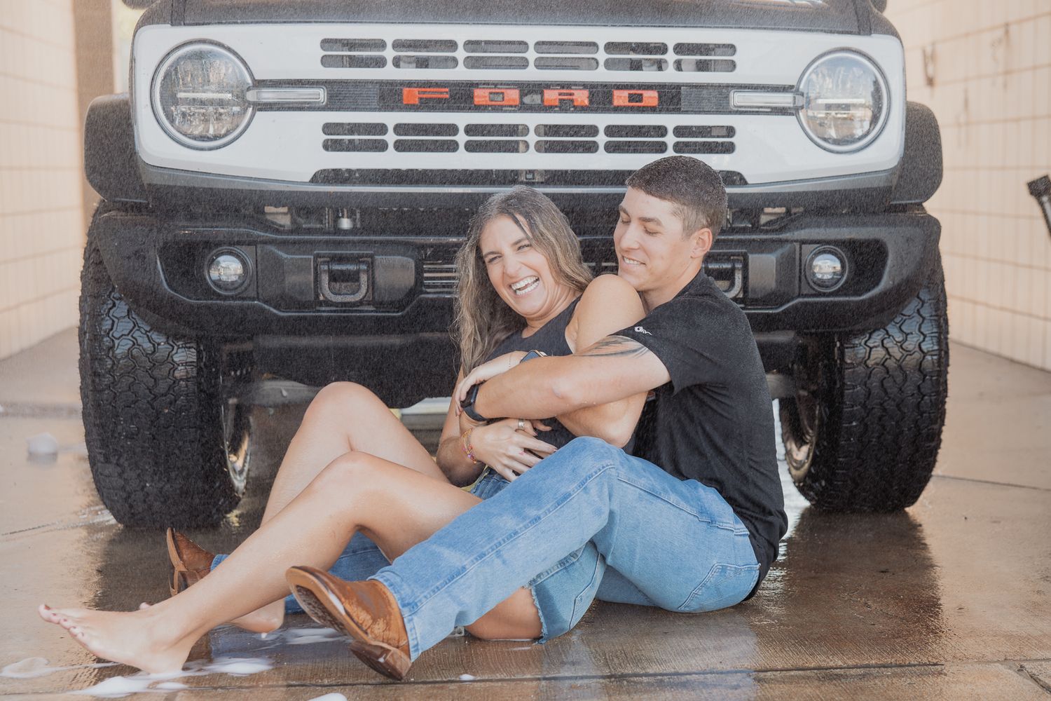 Couple poses casually in front of white Ford Bronco's distinctive front grille.