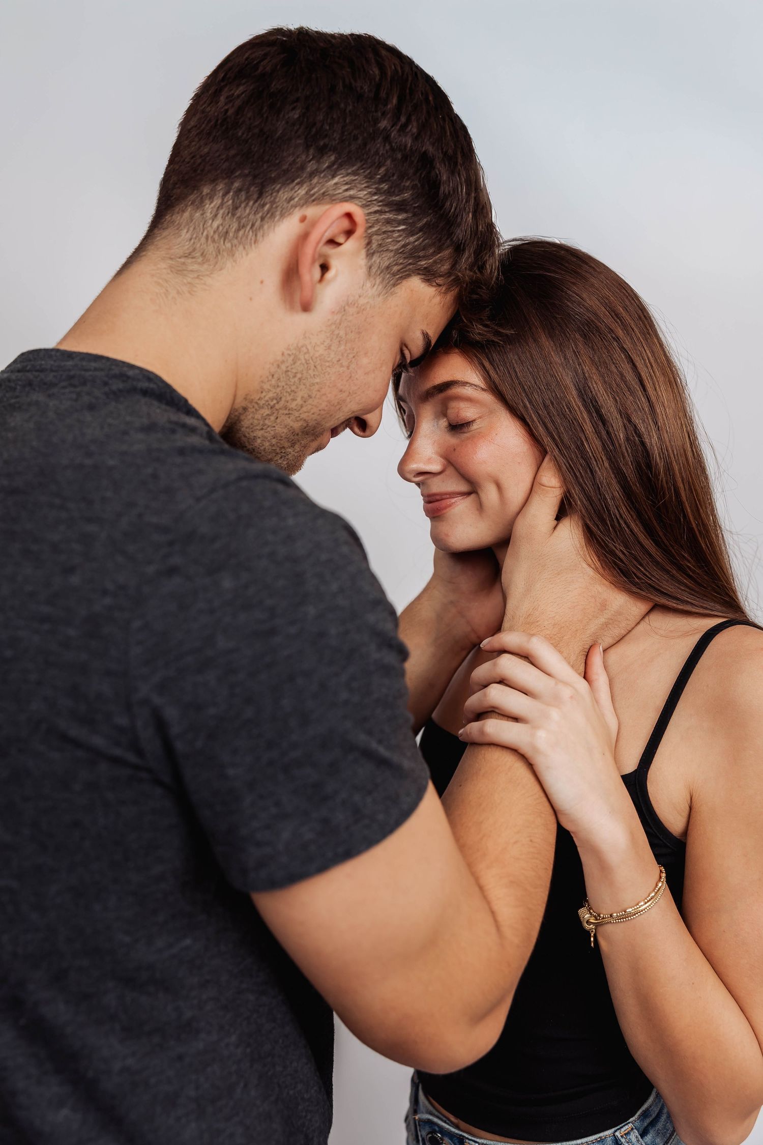 Romantic couple sharing an intimate moment against a light background.