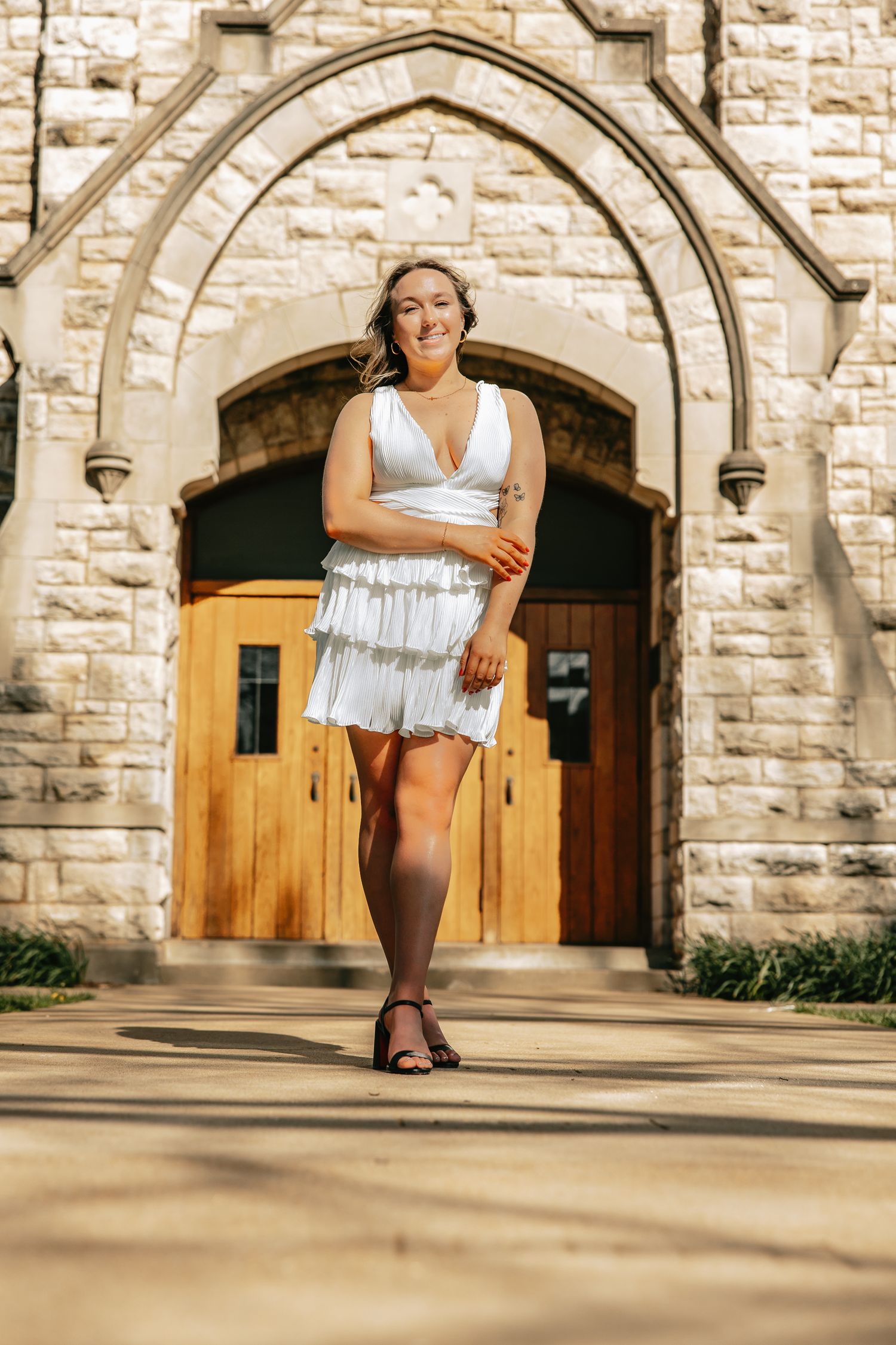 Graduate in white dress poses in front of stone church architecture.