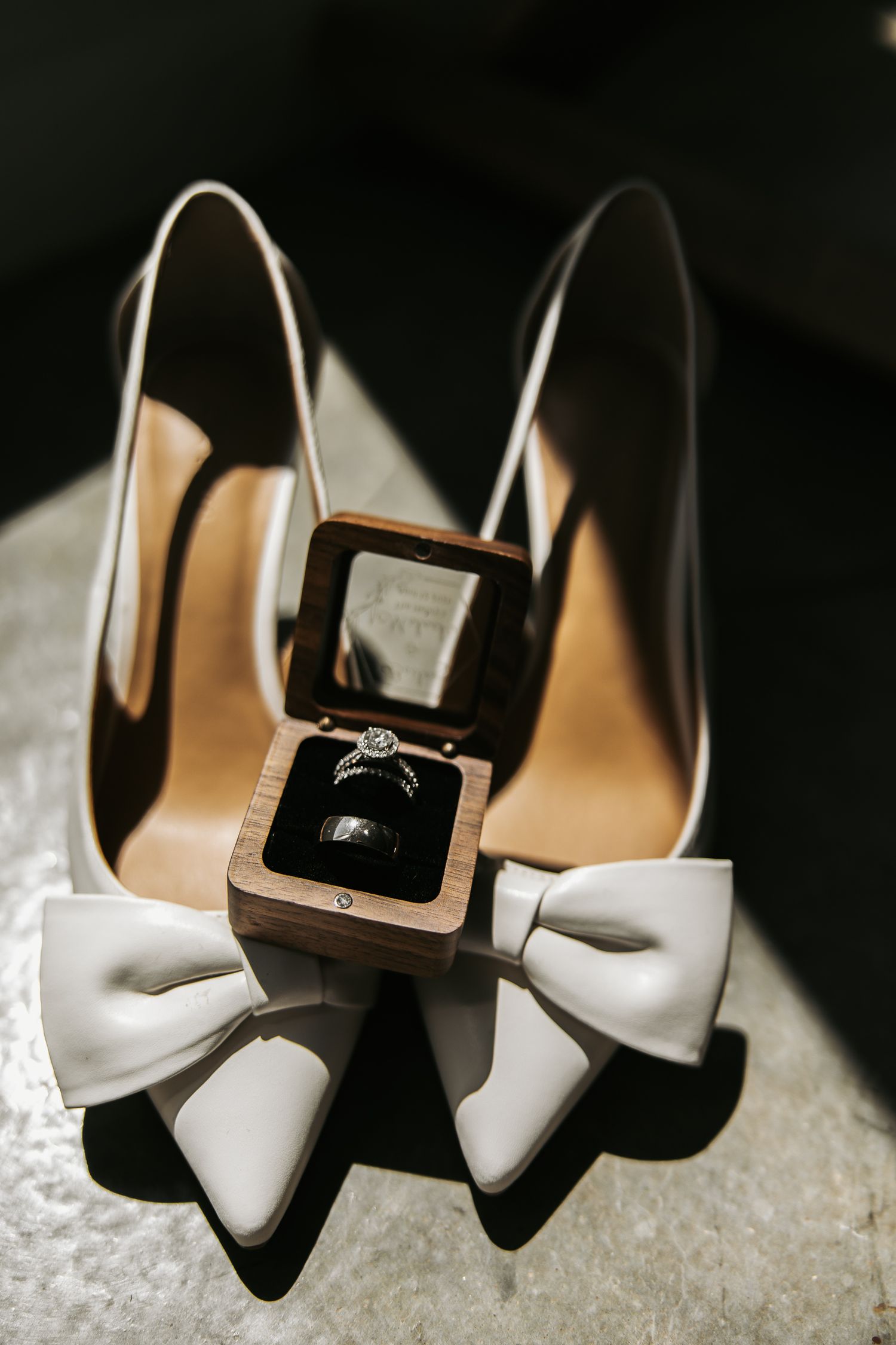 Elegant white bridal heels with decorative buckles photographed against dark background.
