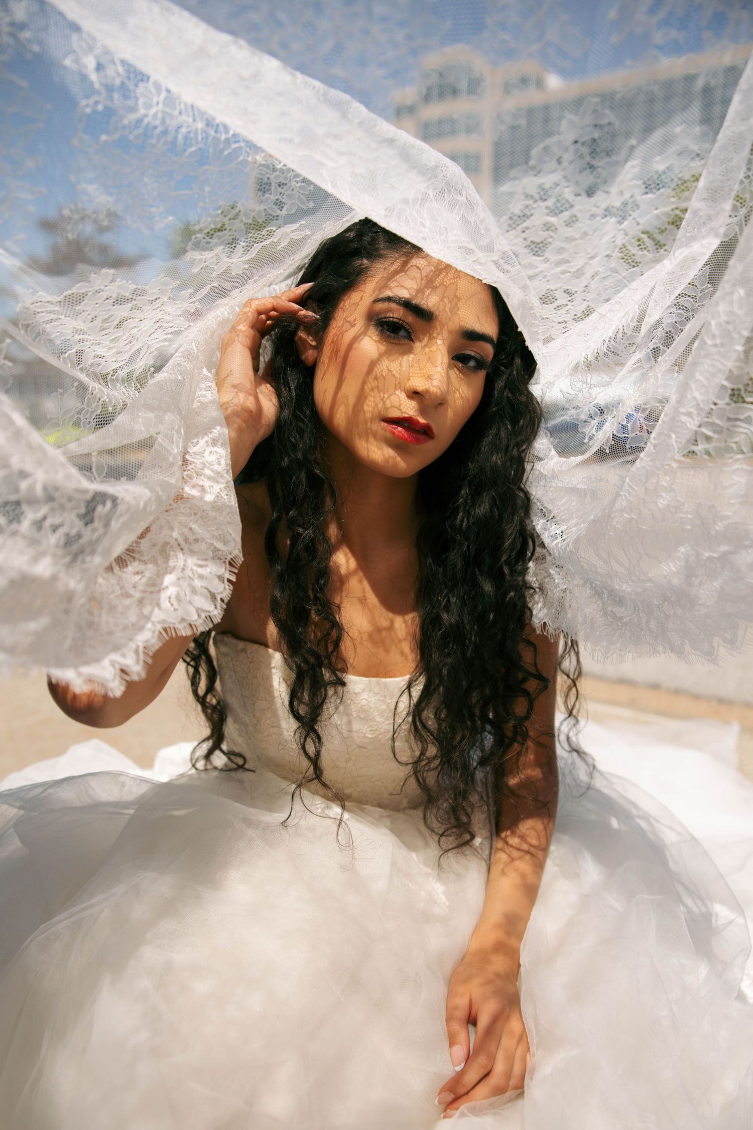 Beautiful bride with long dark hair seated under flowing lace veil in white ball gown wedding dress.