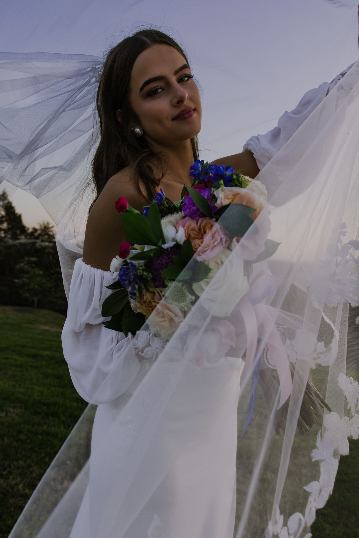 Artistic bridal portraits featuring flowing white fabric and colorful florals against a dusky sky.