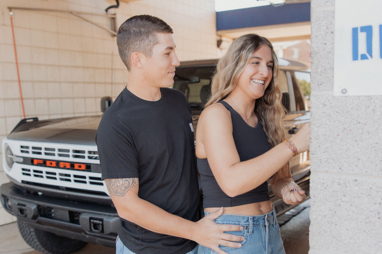 A couple embracing in a covered parking area with vehicles visible in background.