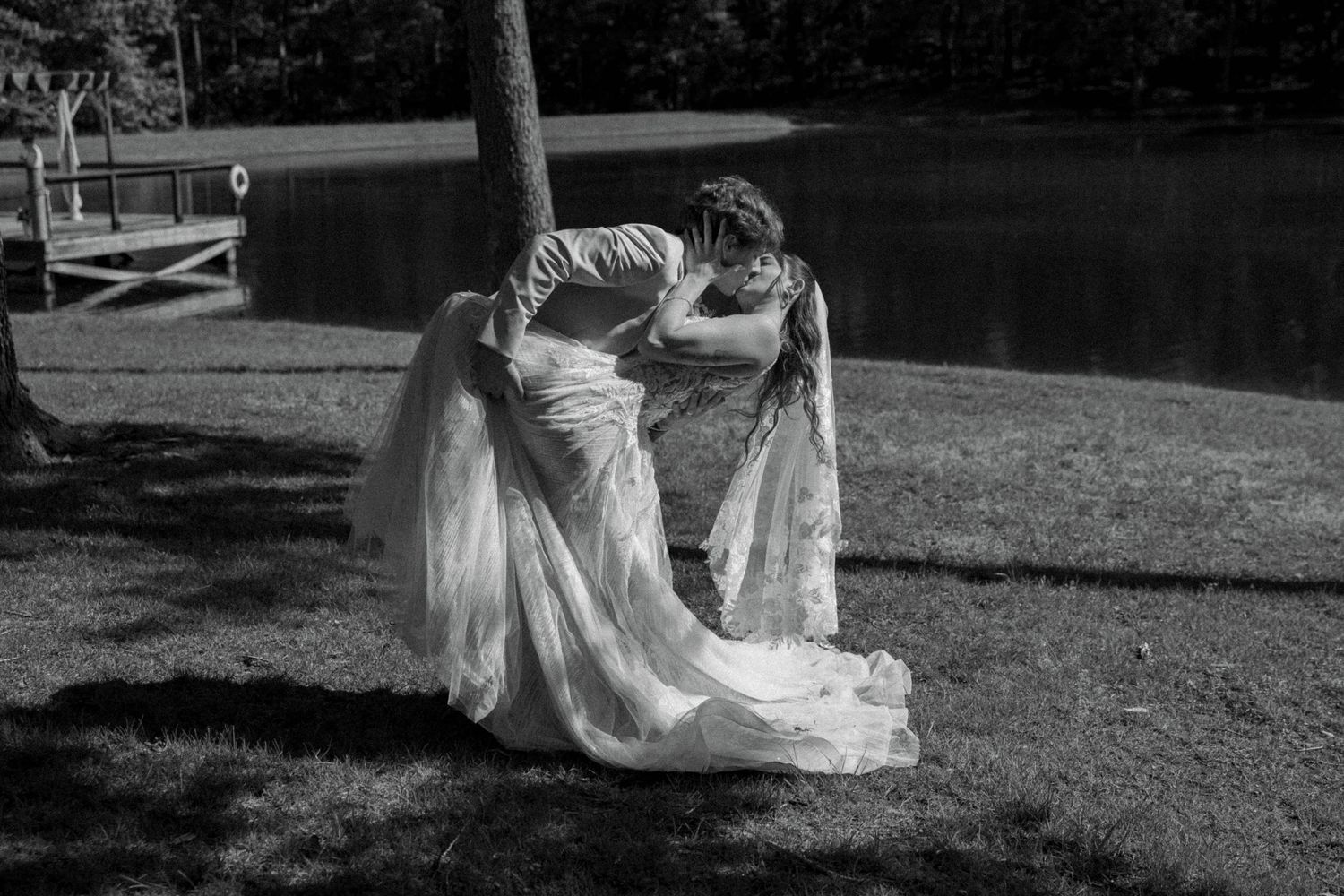 Black and white photo of a bride in a flowing gown dancing near a serene lakeside setting.