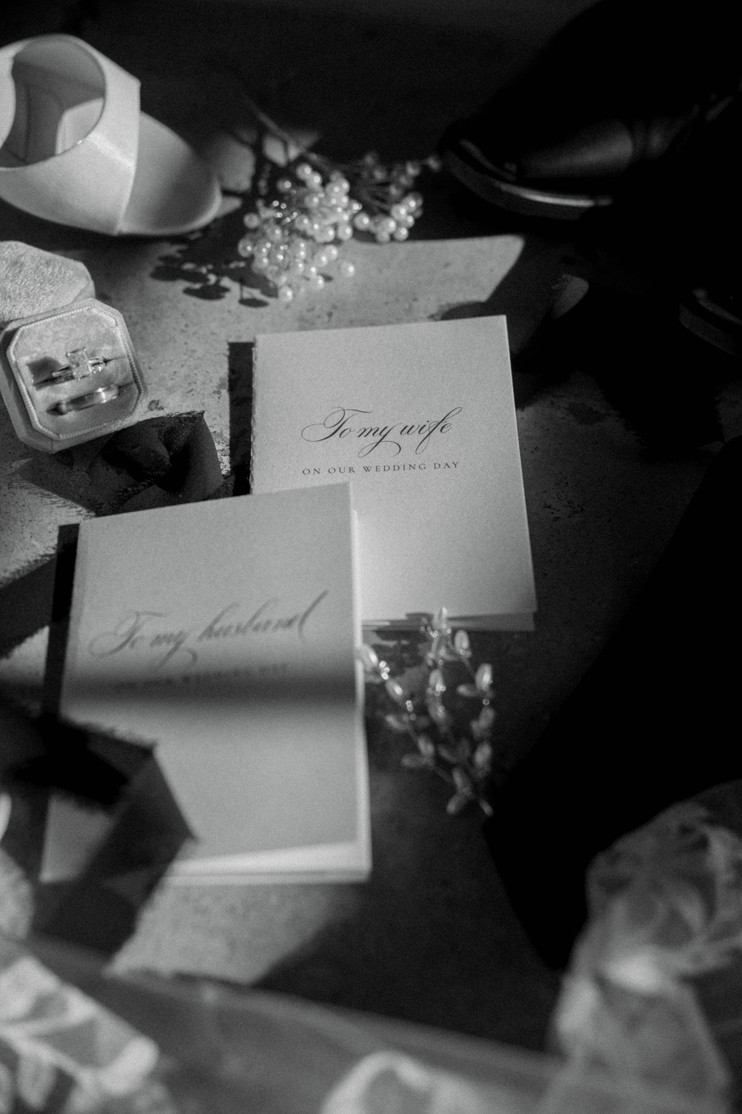 Black and white photo of wedding cards addressed to my wife and husband, with rings and pearl flowers on a table.