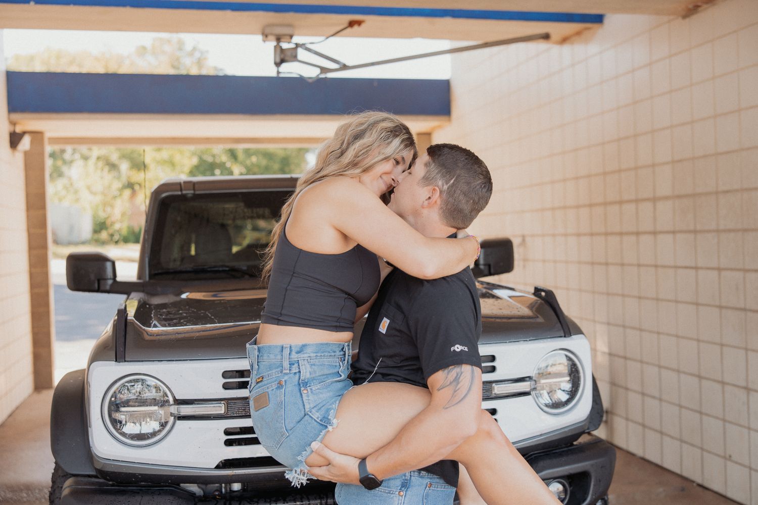 Romantic couple embraces against a white wall with a parked truck in the background.