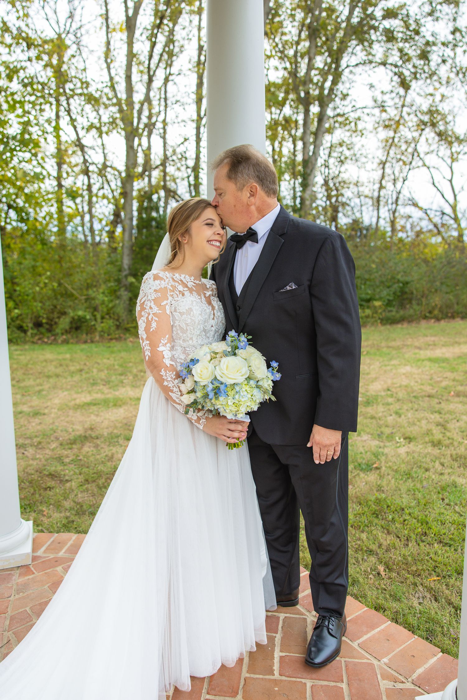 Joyful wedding couple shares intimate moment on brick patio with white columns.