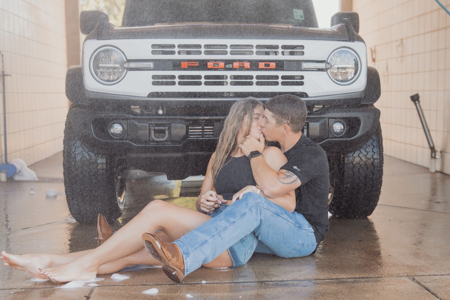 Couple sharing tender moment while sitting in front of modified Ford Bronco.