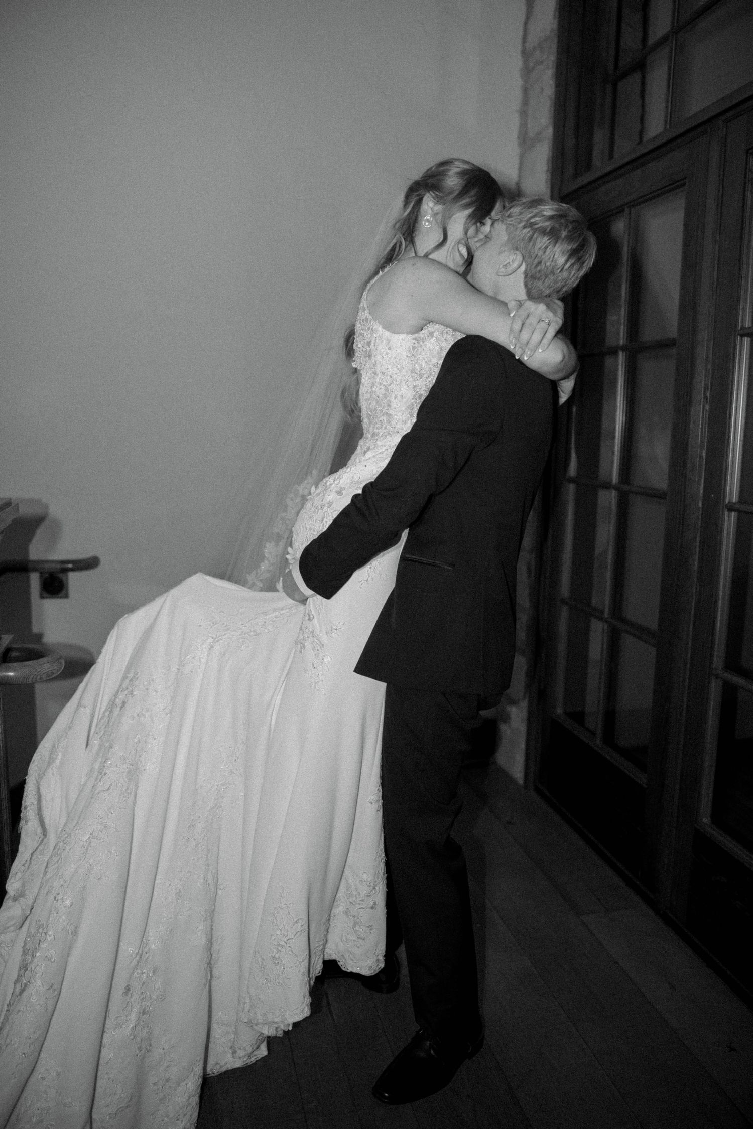 Black and white photo of a bride and groom sharing a romantic kiss on their wedding day.