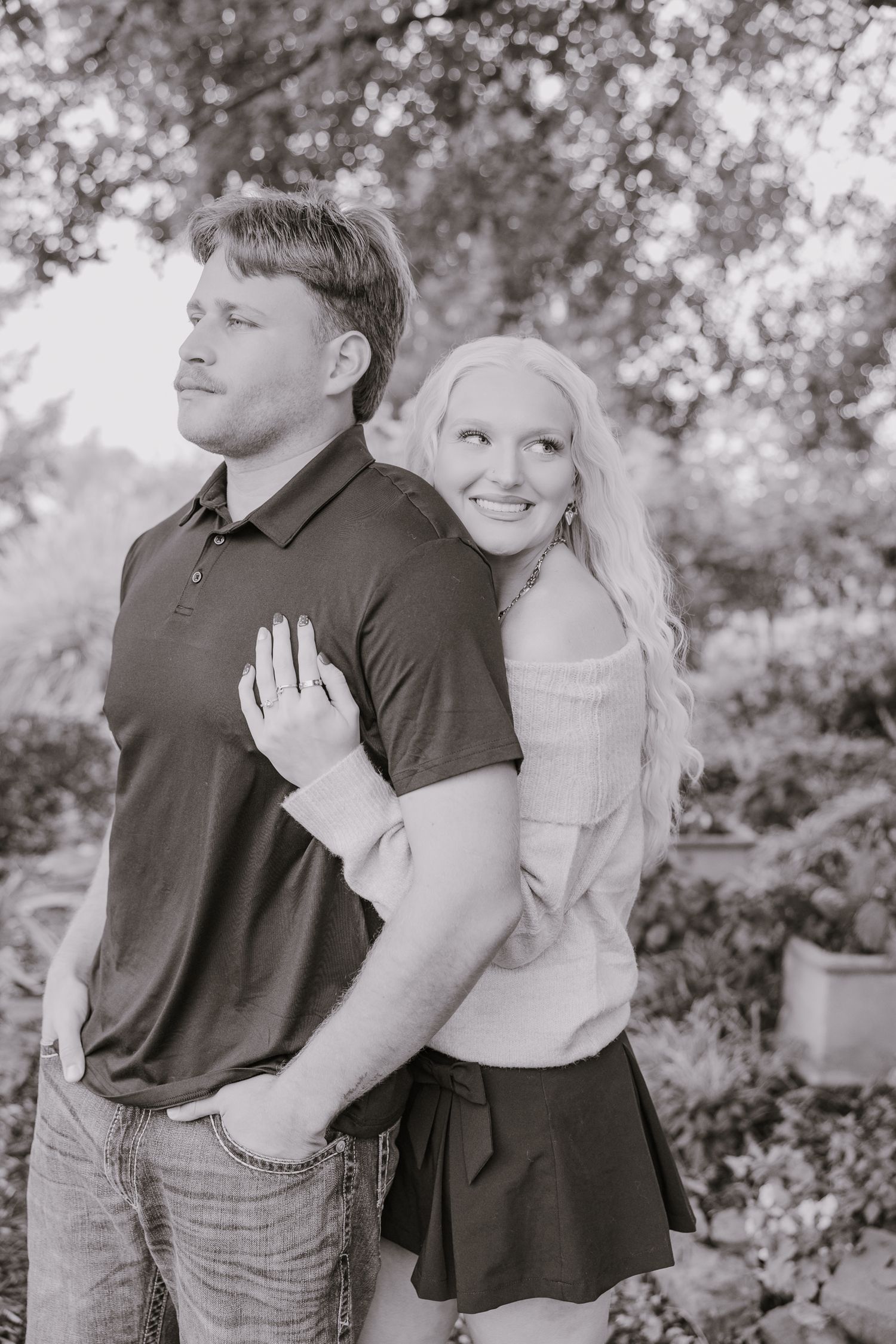 Black and white engagement photo showing a joyful couple posing in a garden setting.