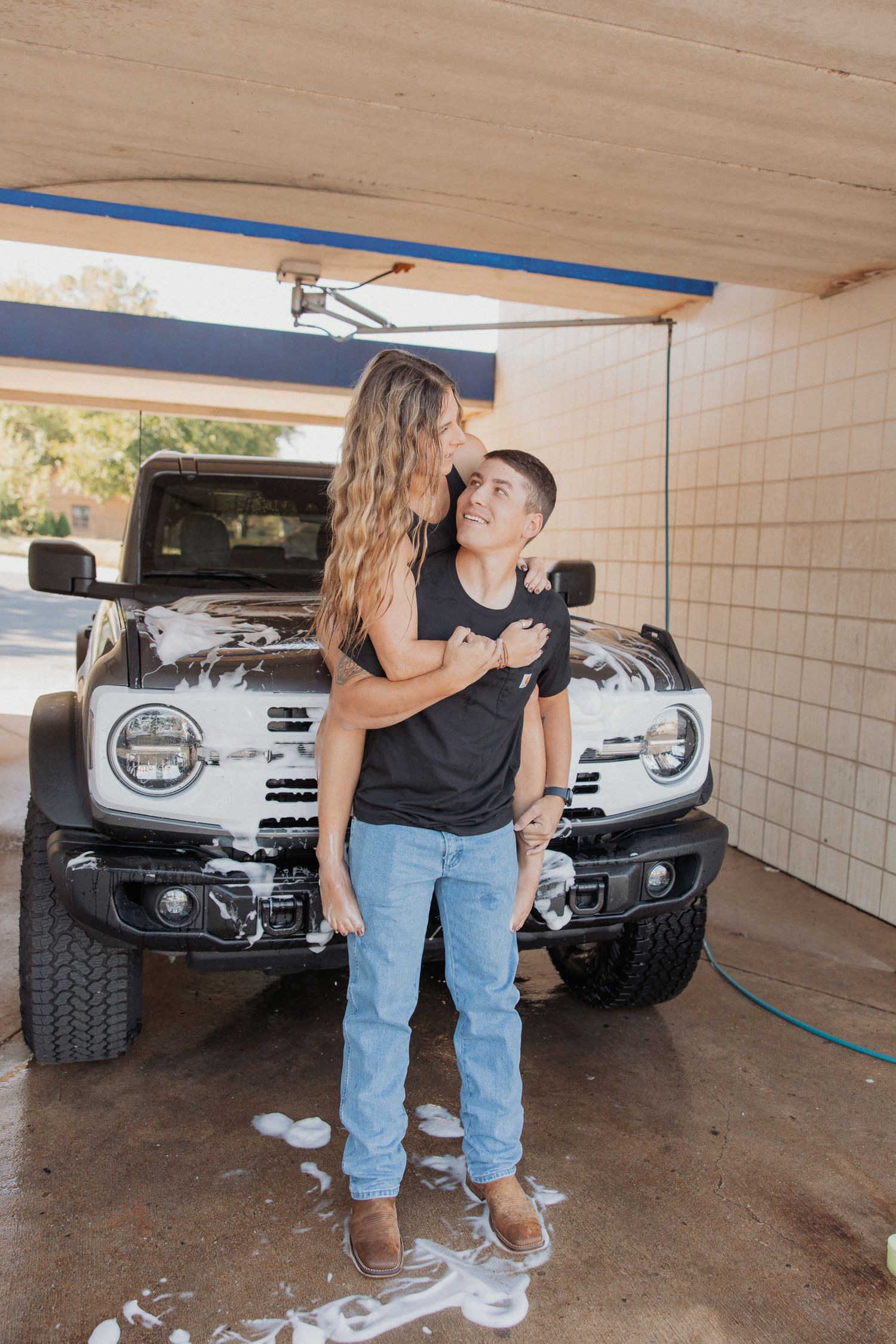 A couple embraces near a parked silver truck in a covered carport area.