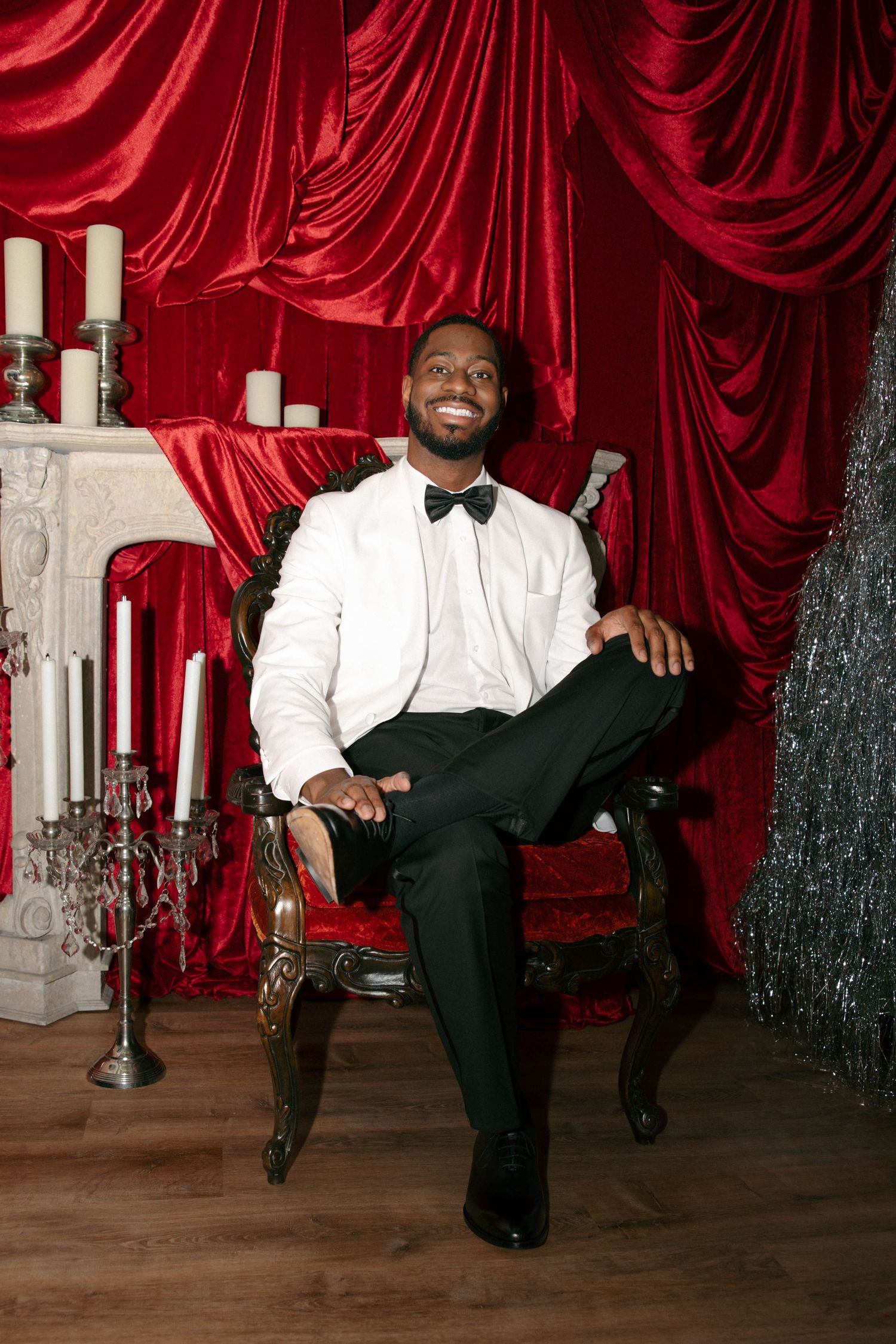 Groomsmen in formal attire relaxing against red velvet curtain backdrop.