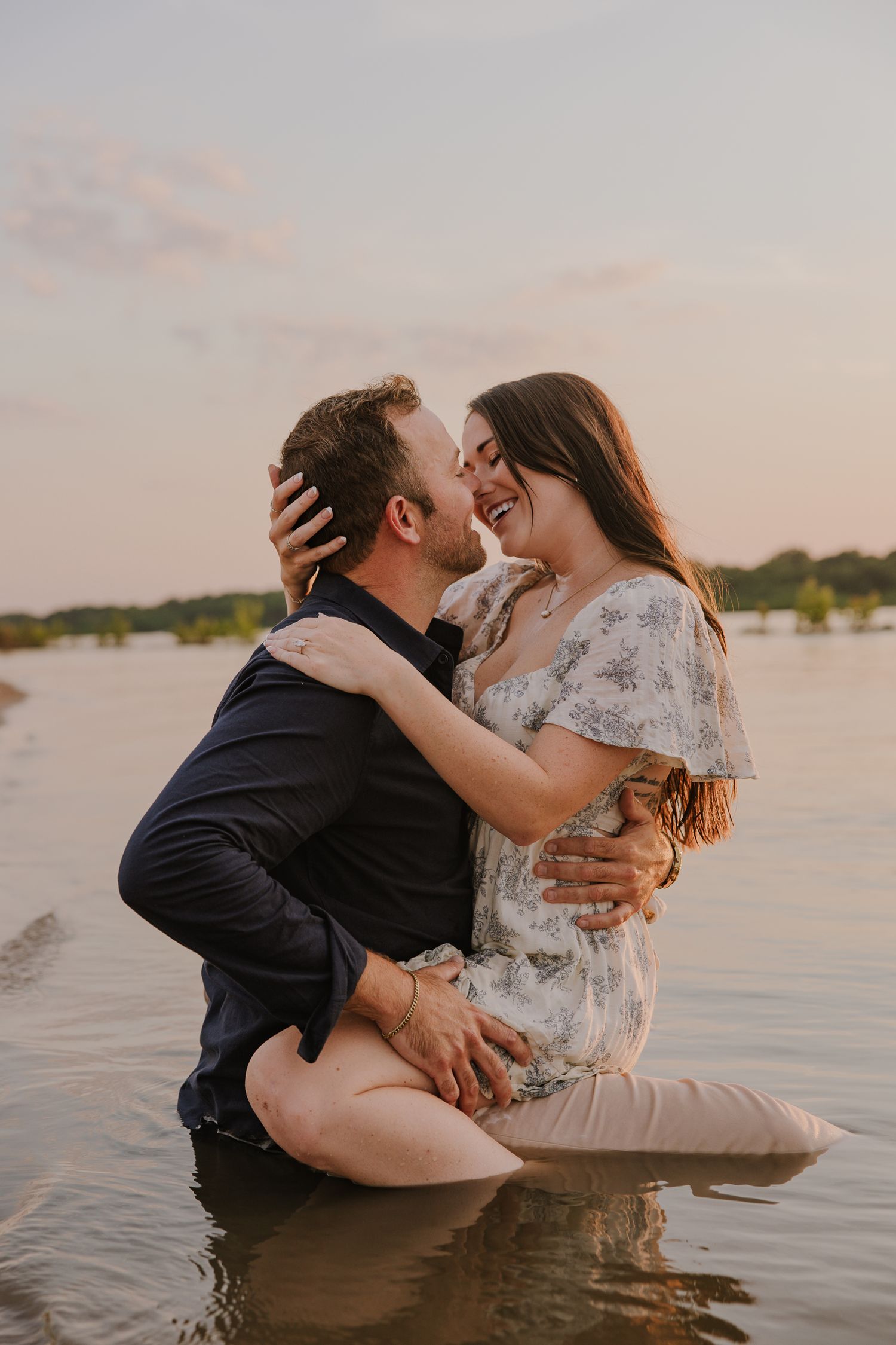 Playful couple splashing in lake water during sunset photography session.