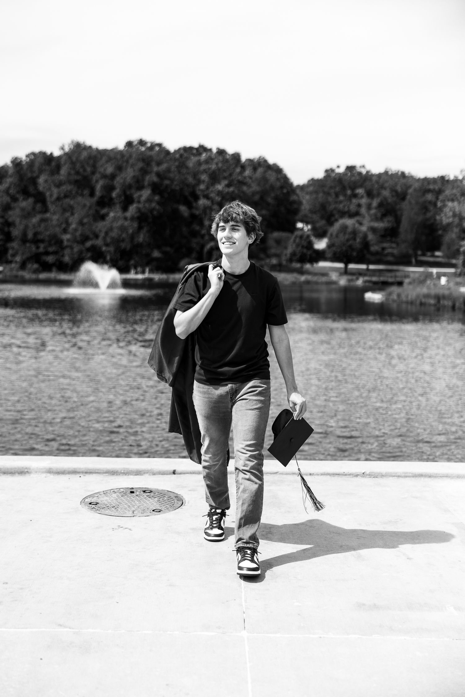 A graduate walks confidently by a lake in black and white photography.