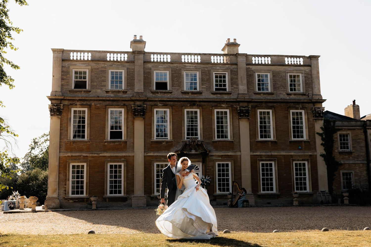 Bride and groom dancing outside a grand Georgian manor house on a sunny wedding day.