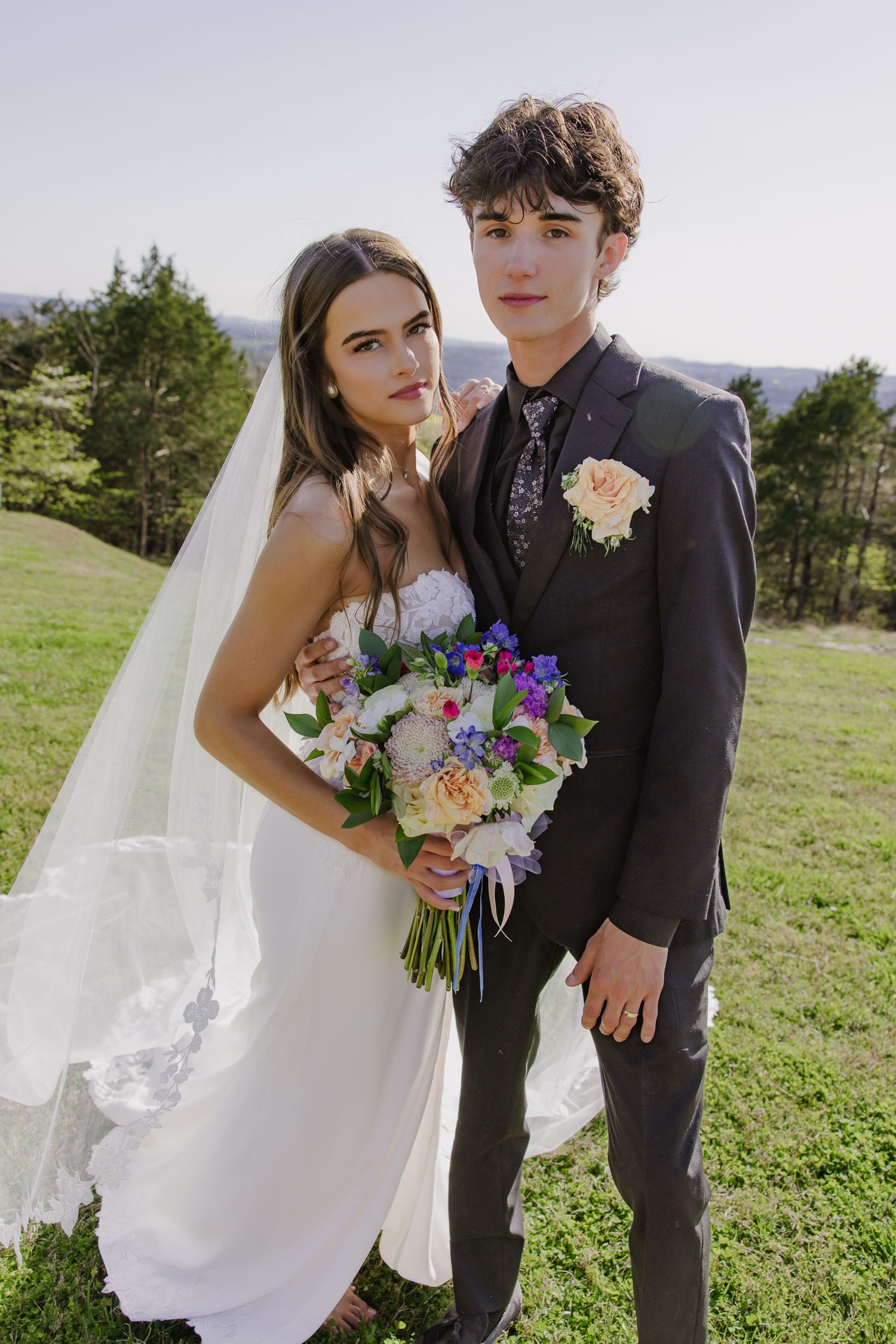 Romantic outdoor wedding photos of a couple in a grassy field with colorful wildflower bouquet.