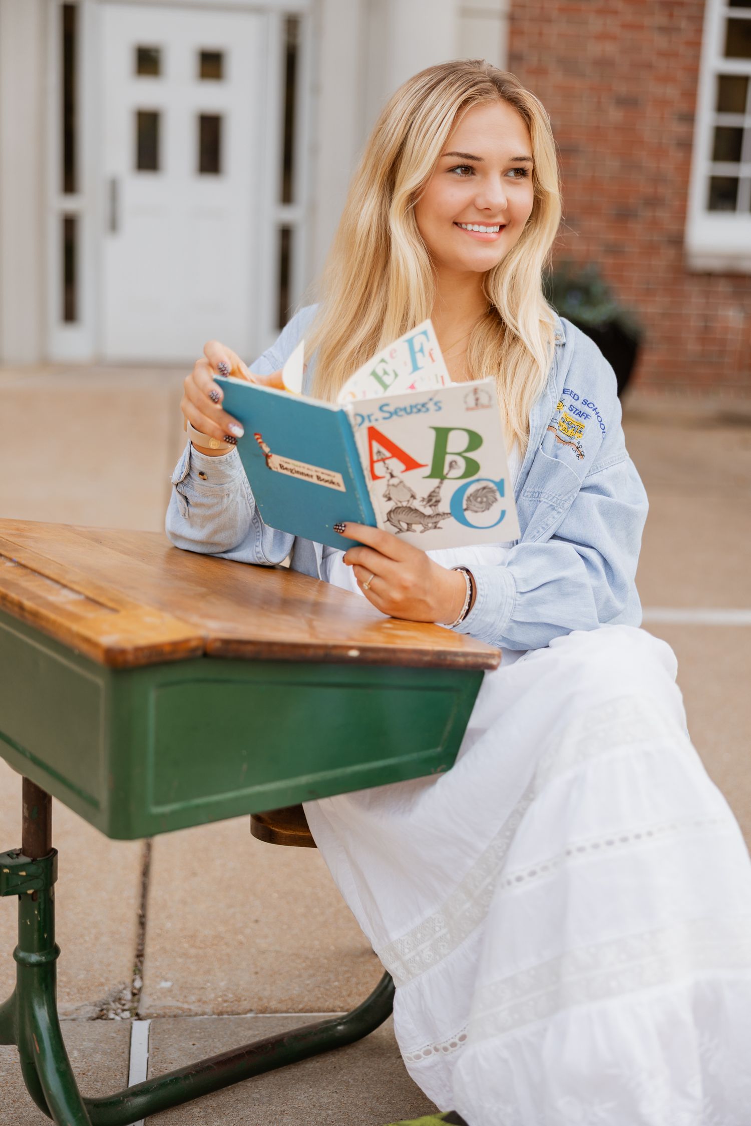 A person in casual attire smiles while reading an educational book at an outdoor desk.