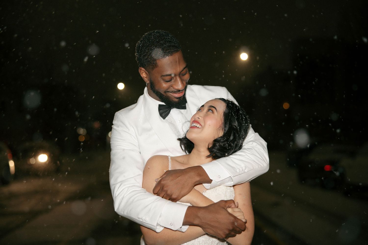 Joyful couple dancing together at night with falling snow and glowing lights.