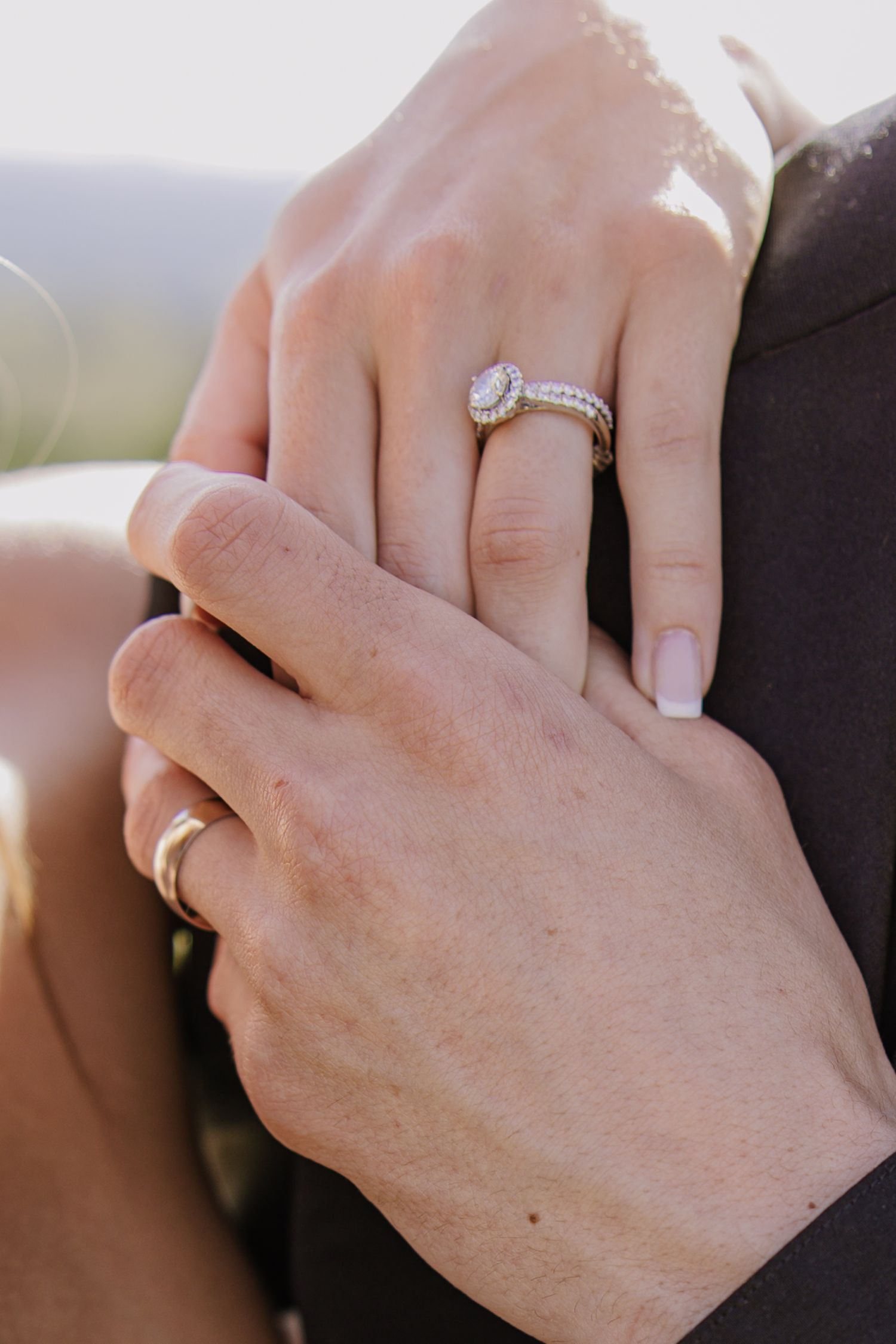 Close-up of wedding rings with diamond engagement ring and gold band on clasped hands.