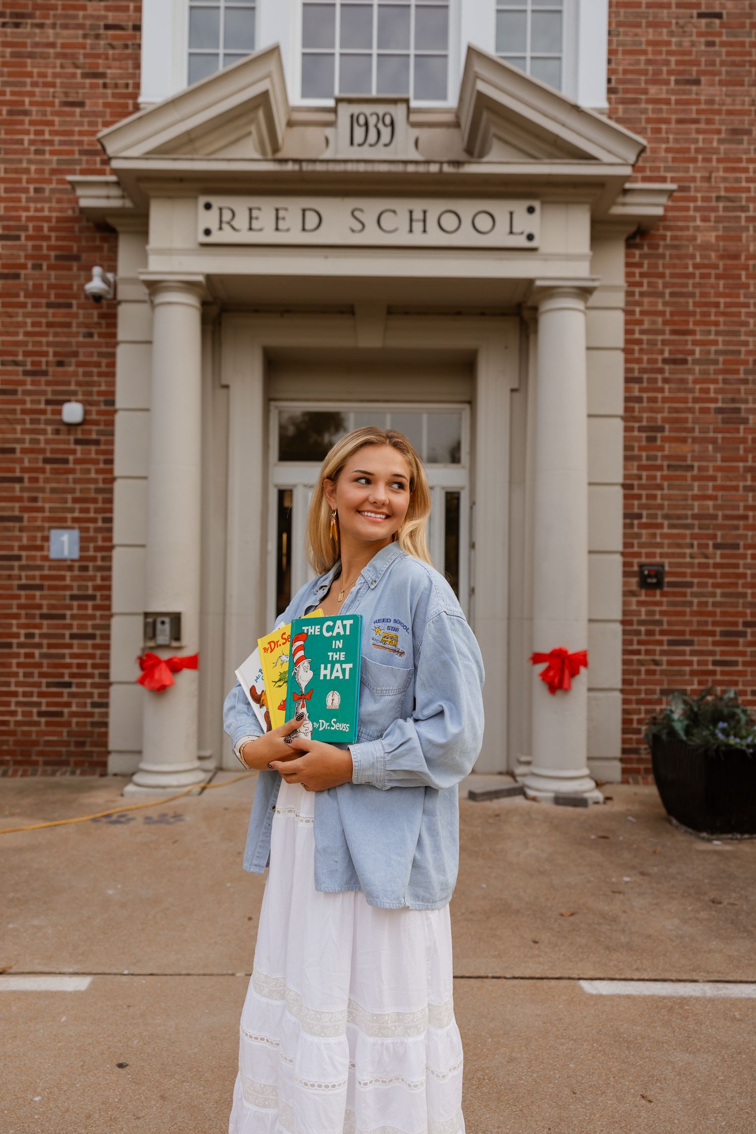 A person poses with children's books outside Reed School's classic brick entrance.