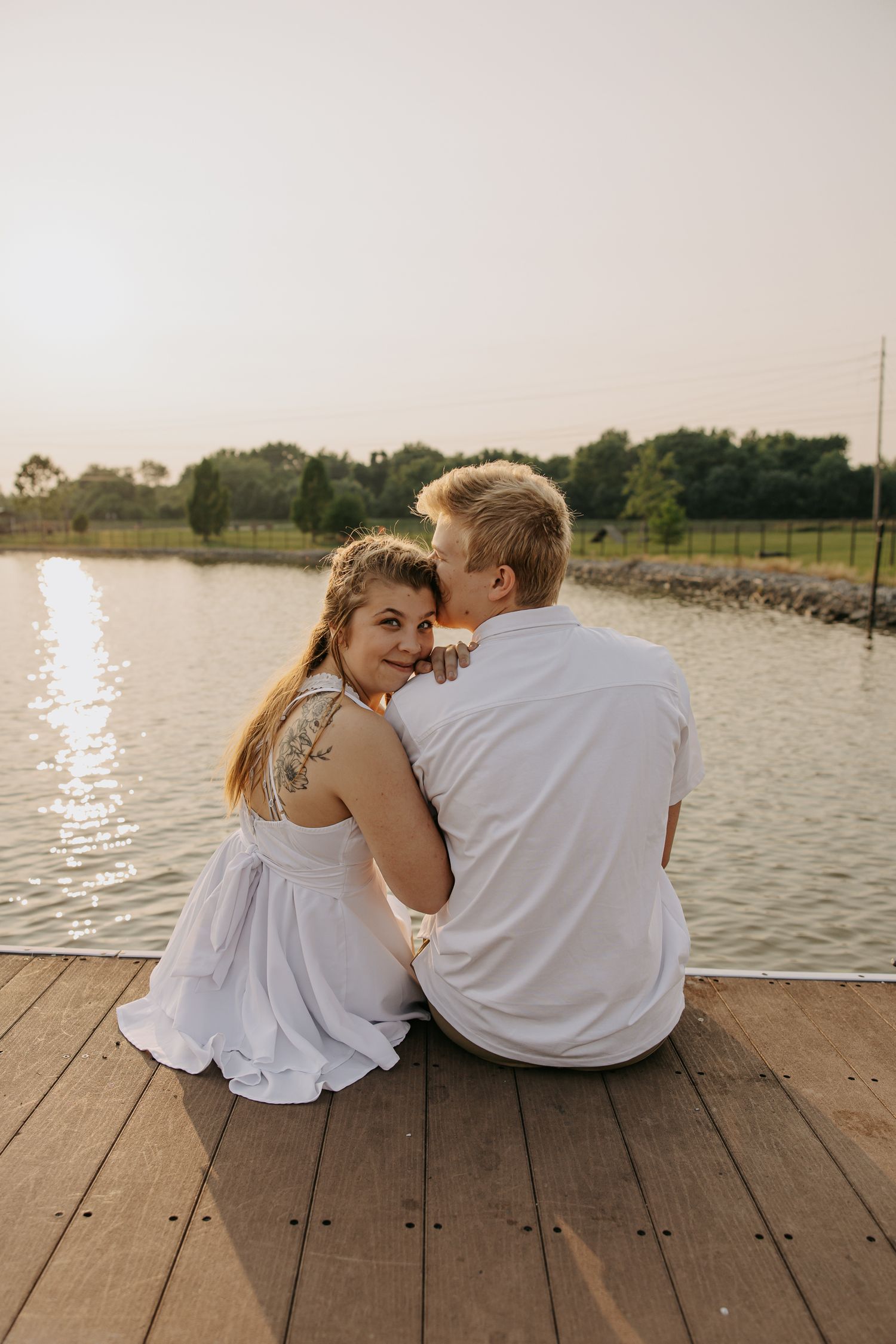 Couple shares intimate moments while sitting on wooden dock by tranquil lake.