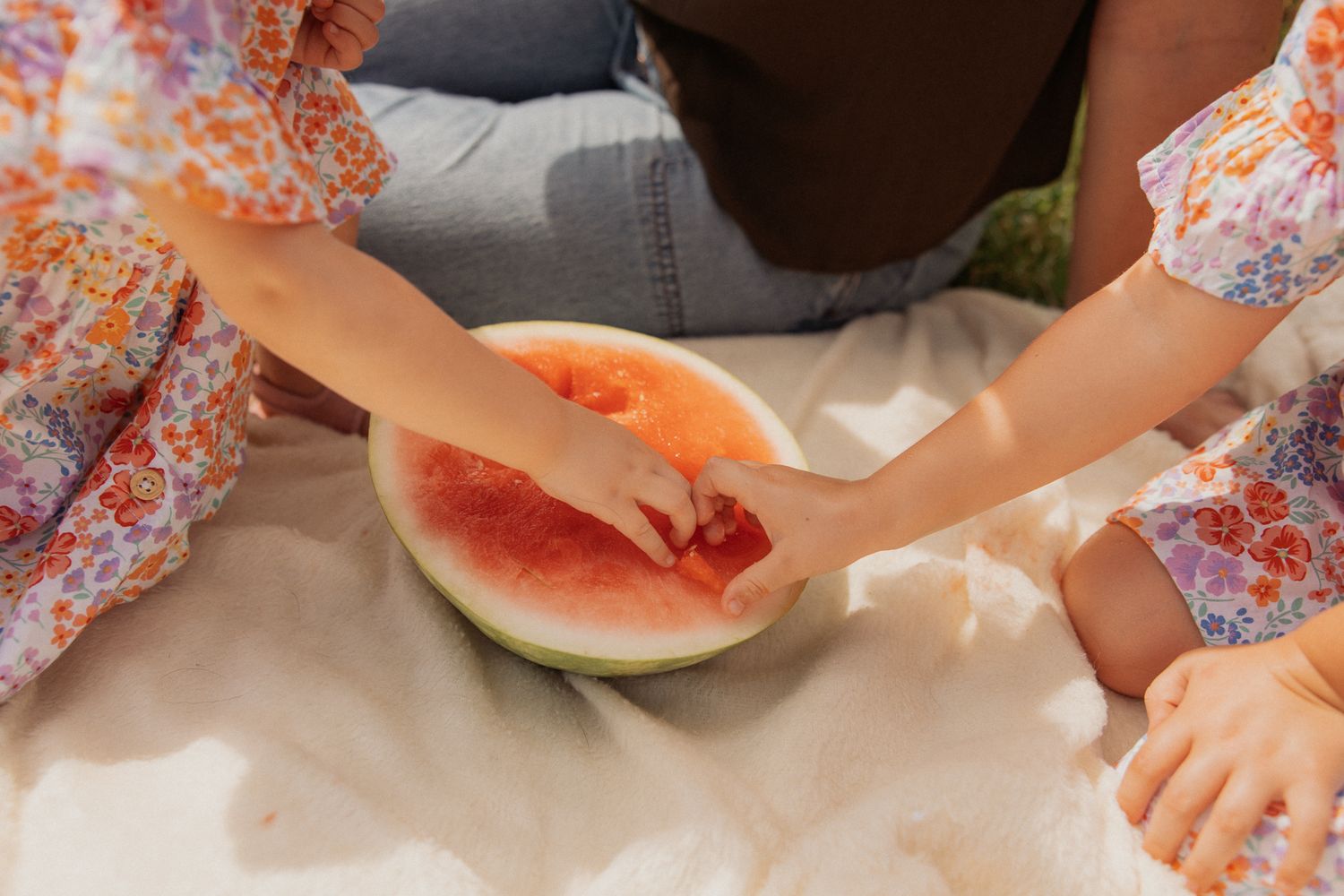 Close-up view of hands reaching for fresh watermelon slices during an outdoor picnic.