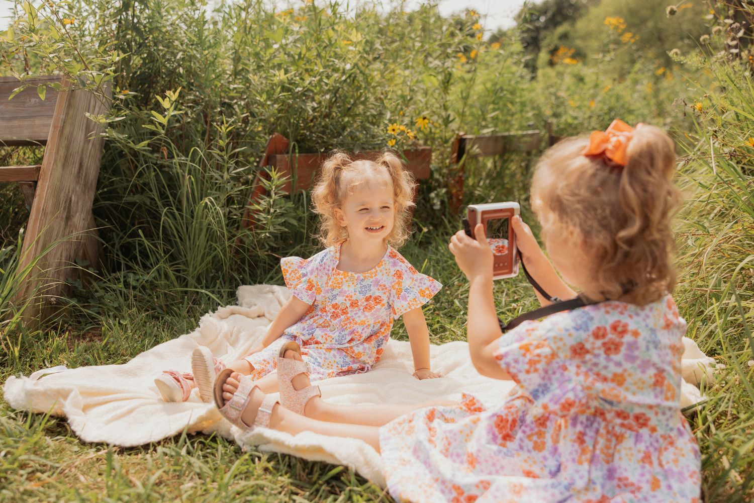 Two matching floral dresses during a picnic photoshoot in a sunny garden setting.