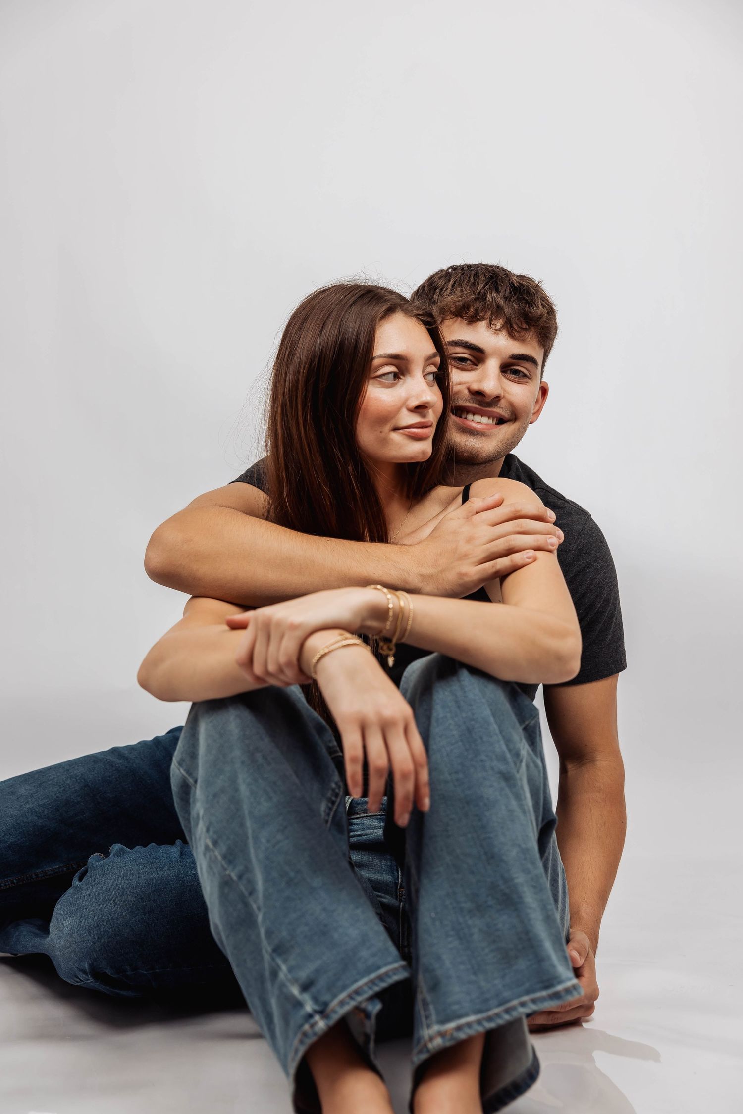 Couple cuddling and laughing while sitting on white studio floor.