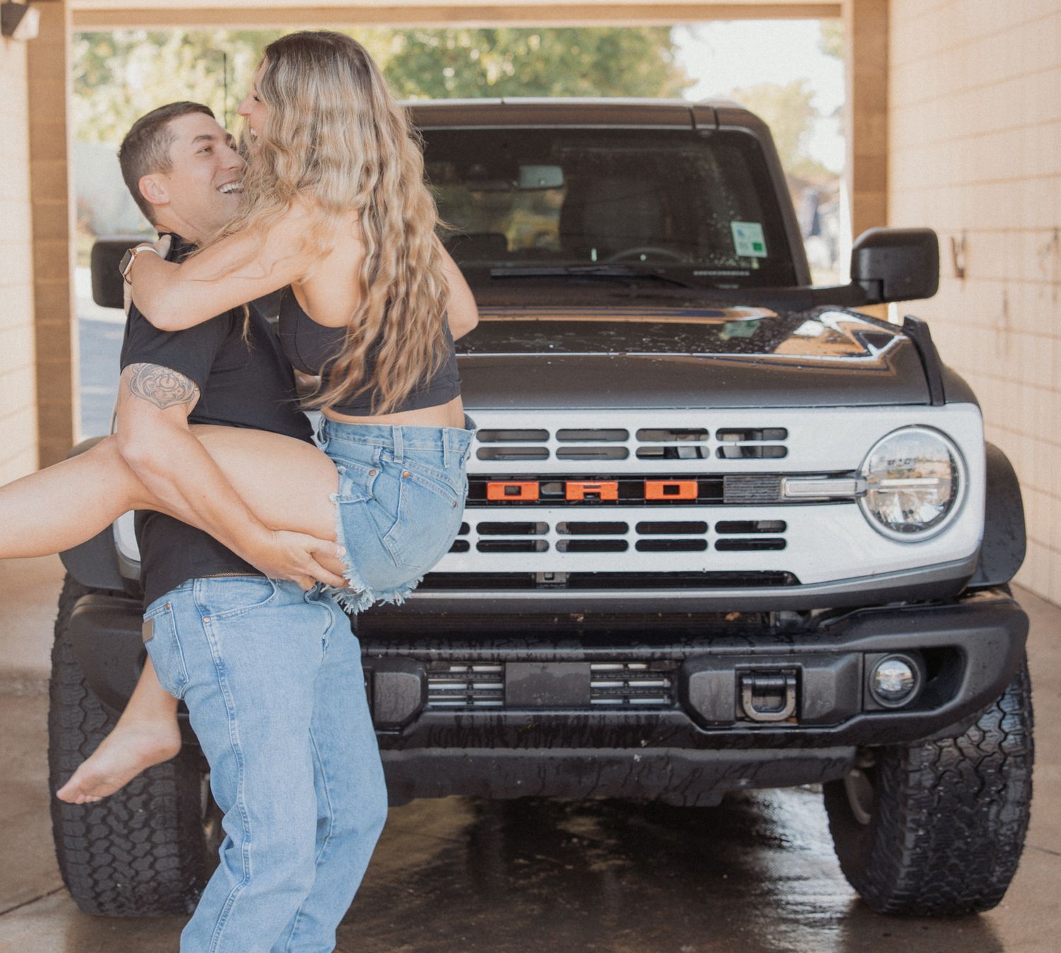 Couple sharing tender moment in front of white bronco truck in covered parking.