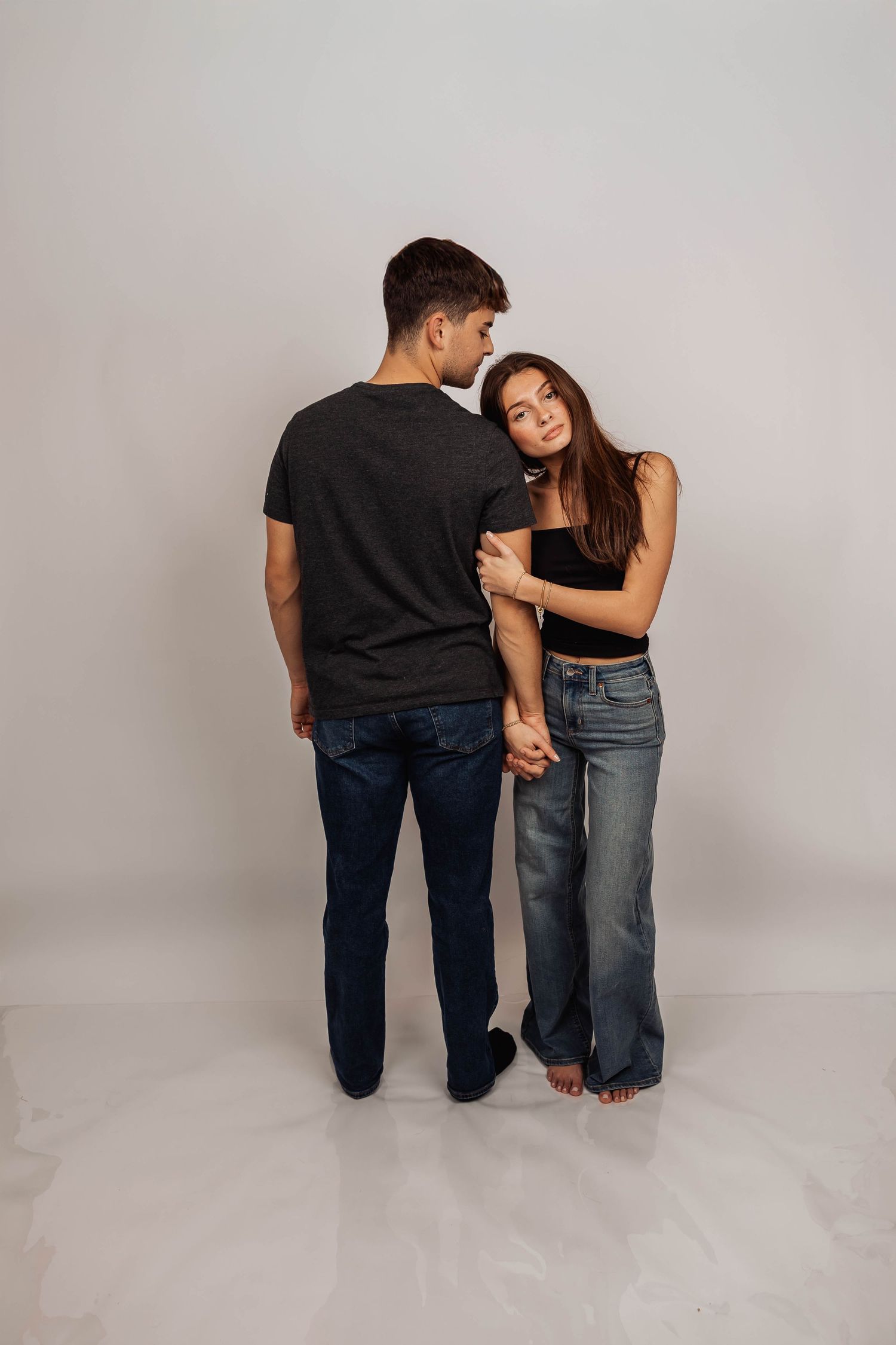 Couple in casual attire poses together against white studio backdrop.