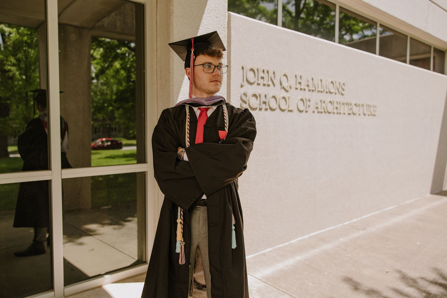 Graduate in academic regalia poses for photos in front of modern campus building.