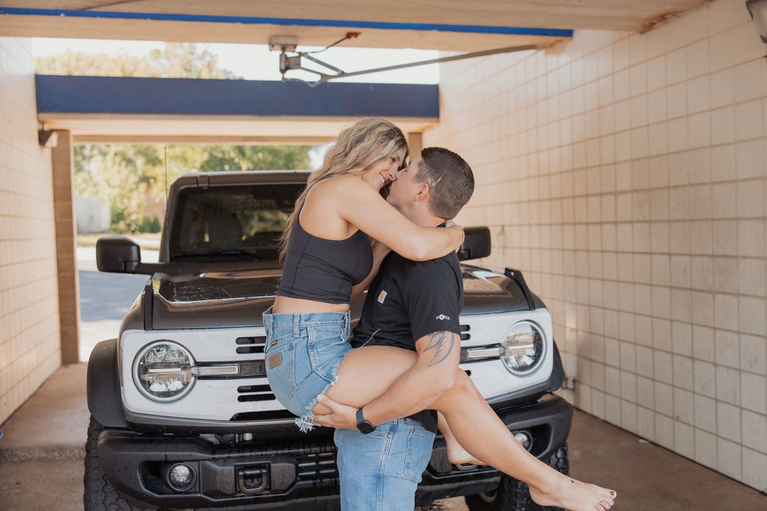Couple embracing in a covered parking area with a white truck visible.