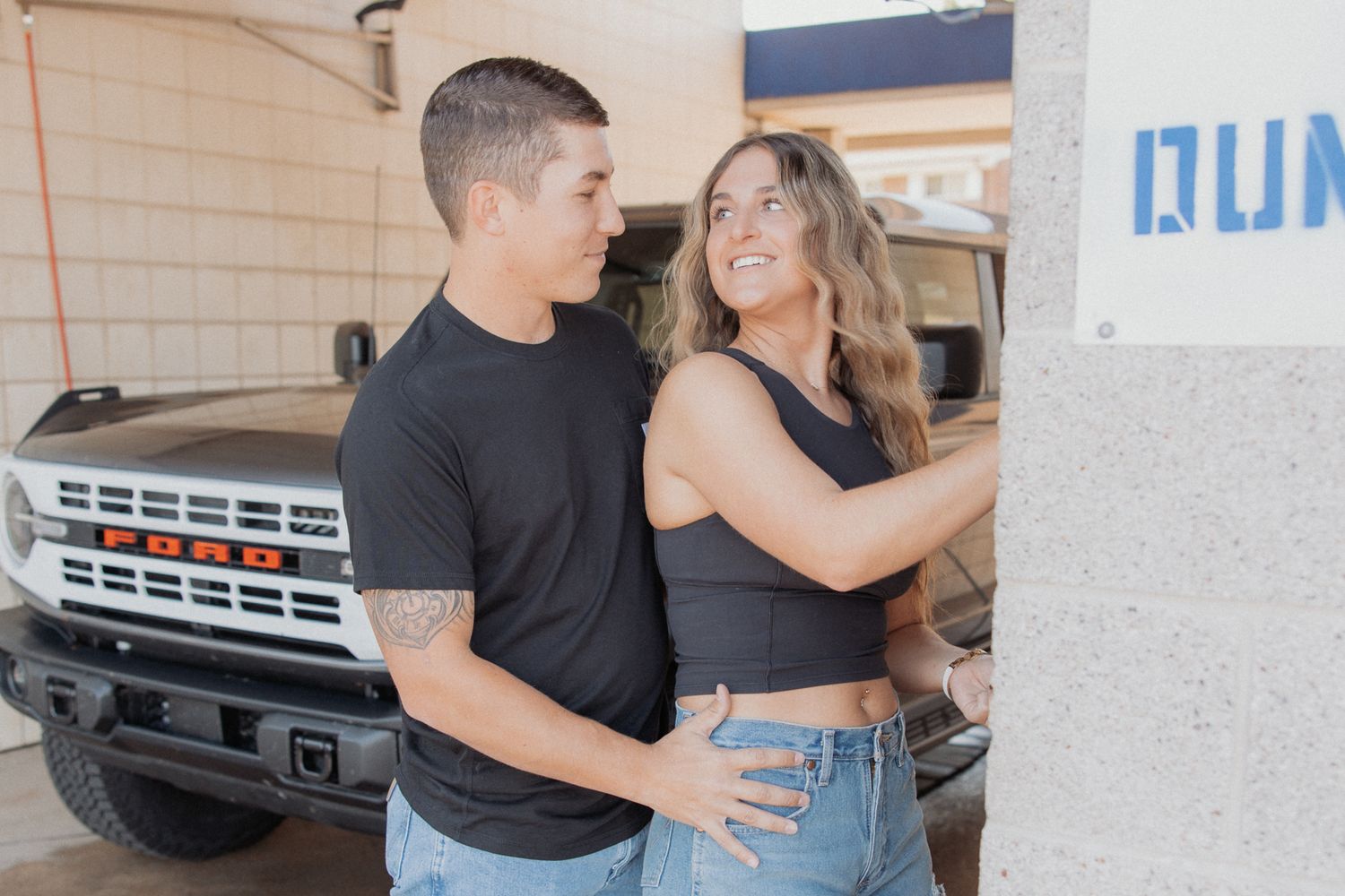 A couple sharing a playful moment in front of parked vehicles.