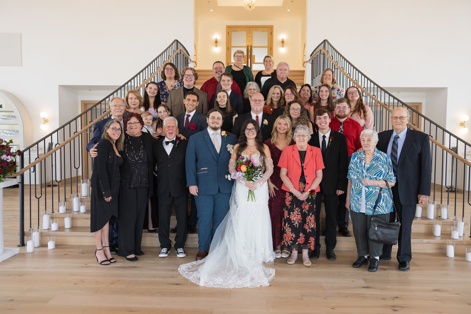 Wedding party and guests gather on grand staircase for group photo.