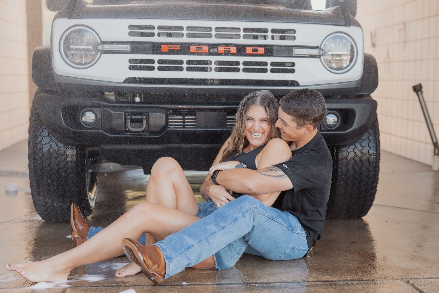 Couple shares affectionate moment while sitting in front of classic Ford Bronco.