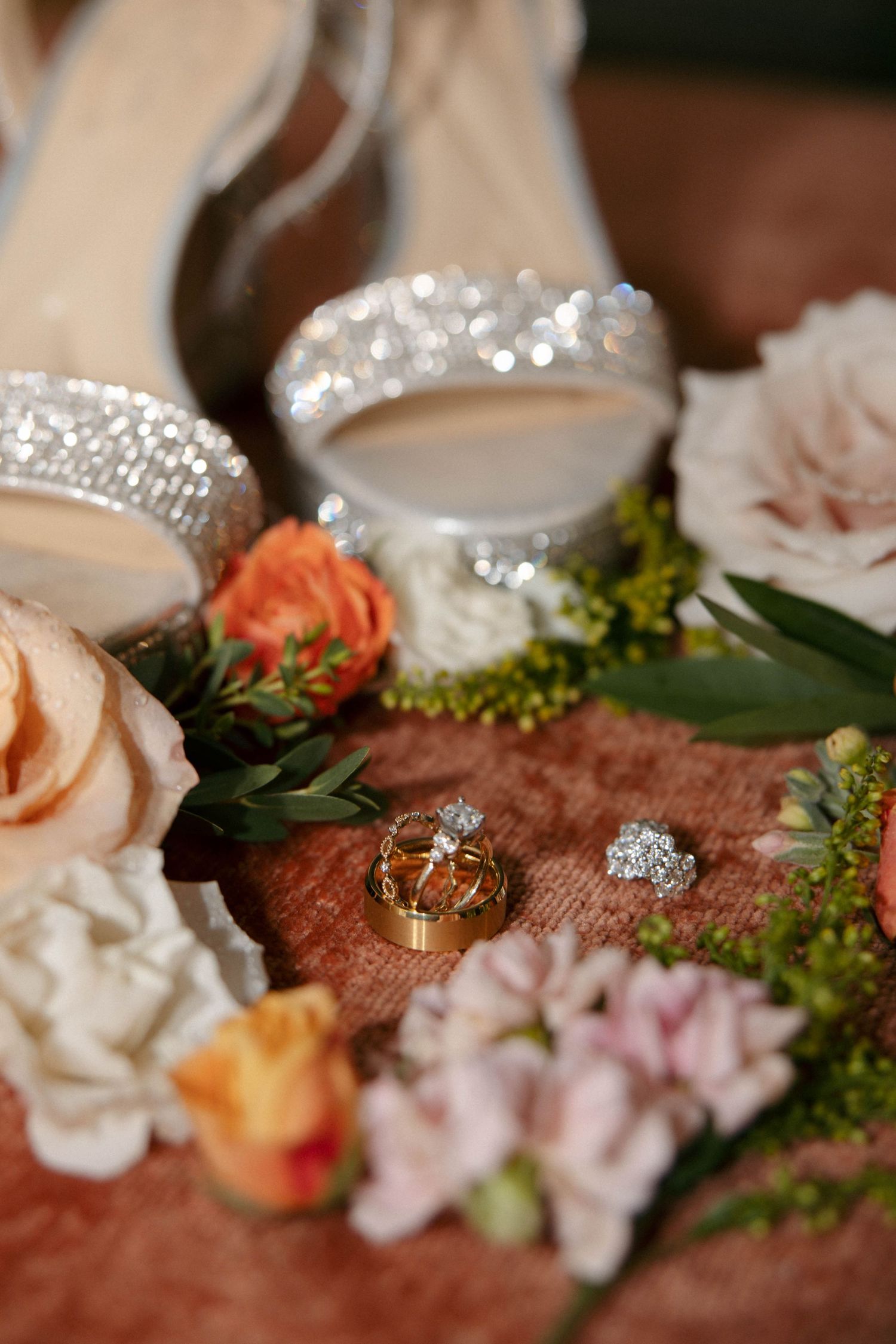 Wedding rings and floral decorations arranged on a textured surface with soft lighting.