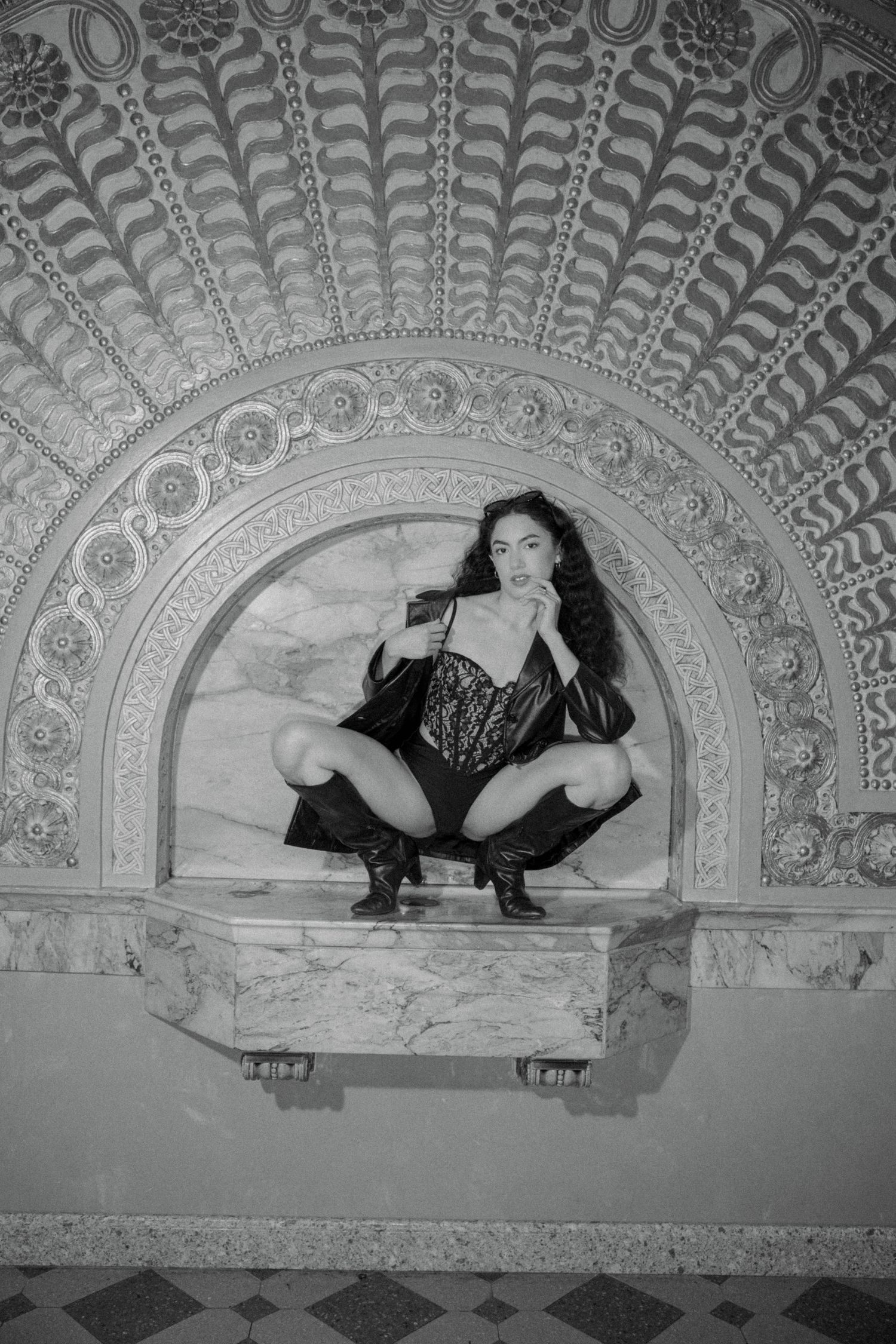 Black and white photo of a woman posing in lace lingerie within an ornate arched marble alcove.