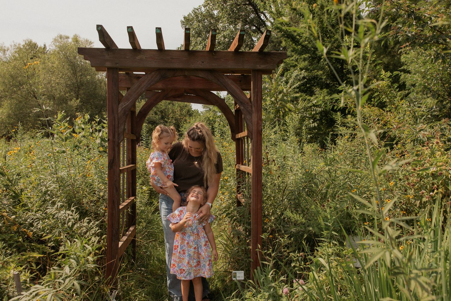 A wooden garden arbor surrounded by lush greenery creates a natural framing in an outdoor setting.