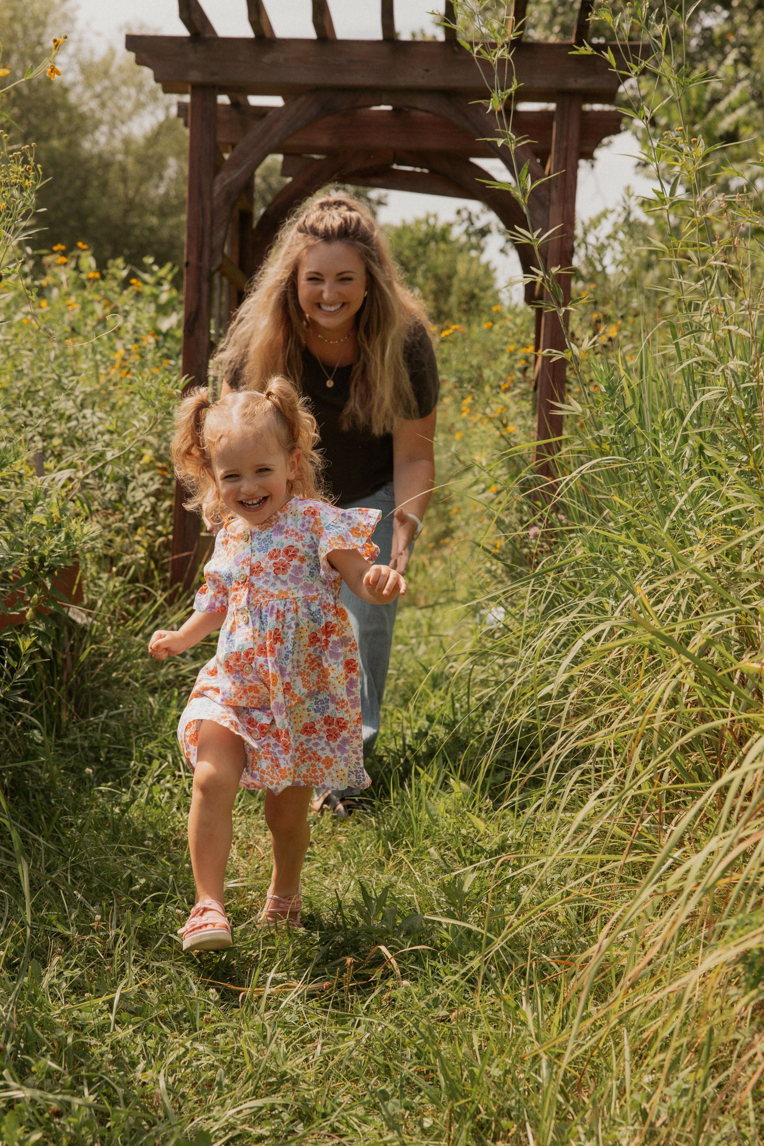 A joyful moment captured under a wooden pergola surrounded by wild summer grasses.
