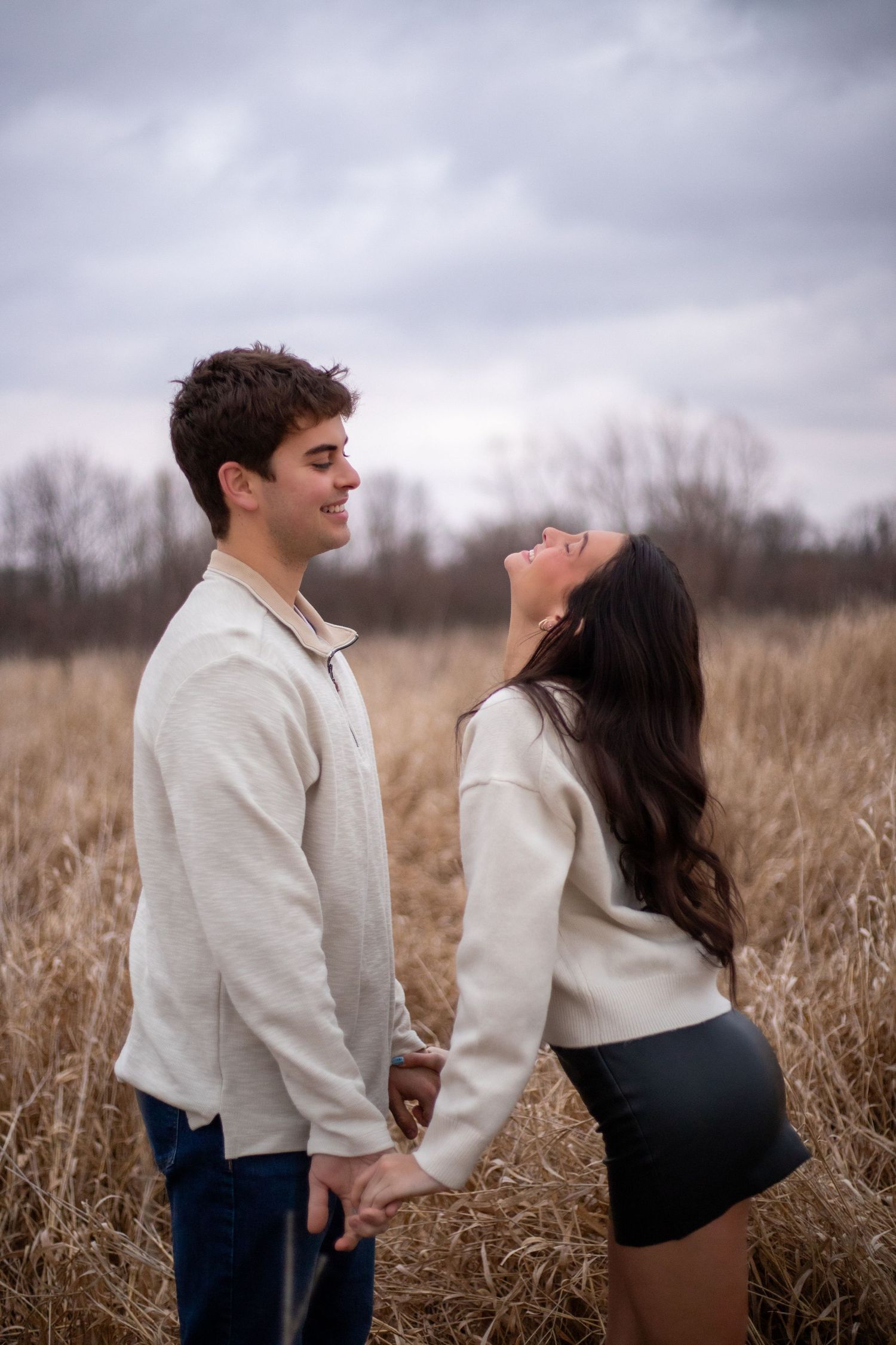 A couple shares an intimate moment in a field of tall brown grass on an overcast day.