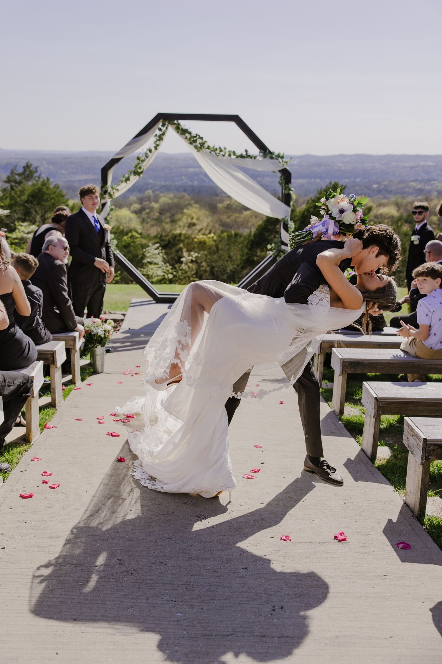Wedding couple poses playfully in front of scenic mountain backdrop during ceremony.