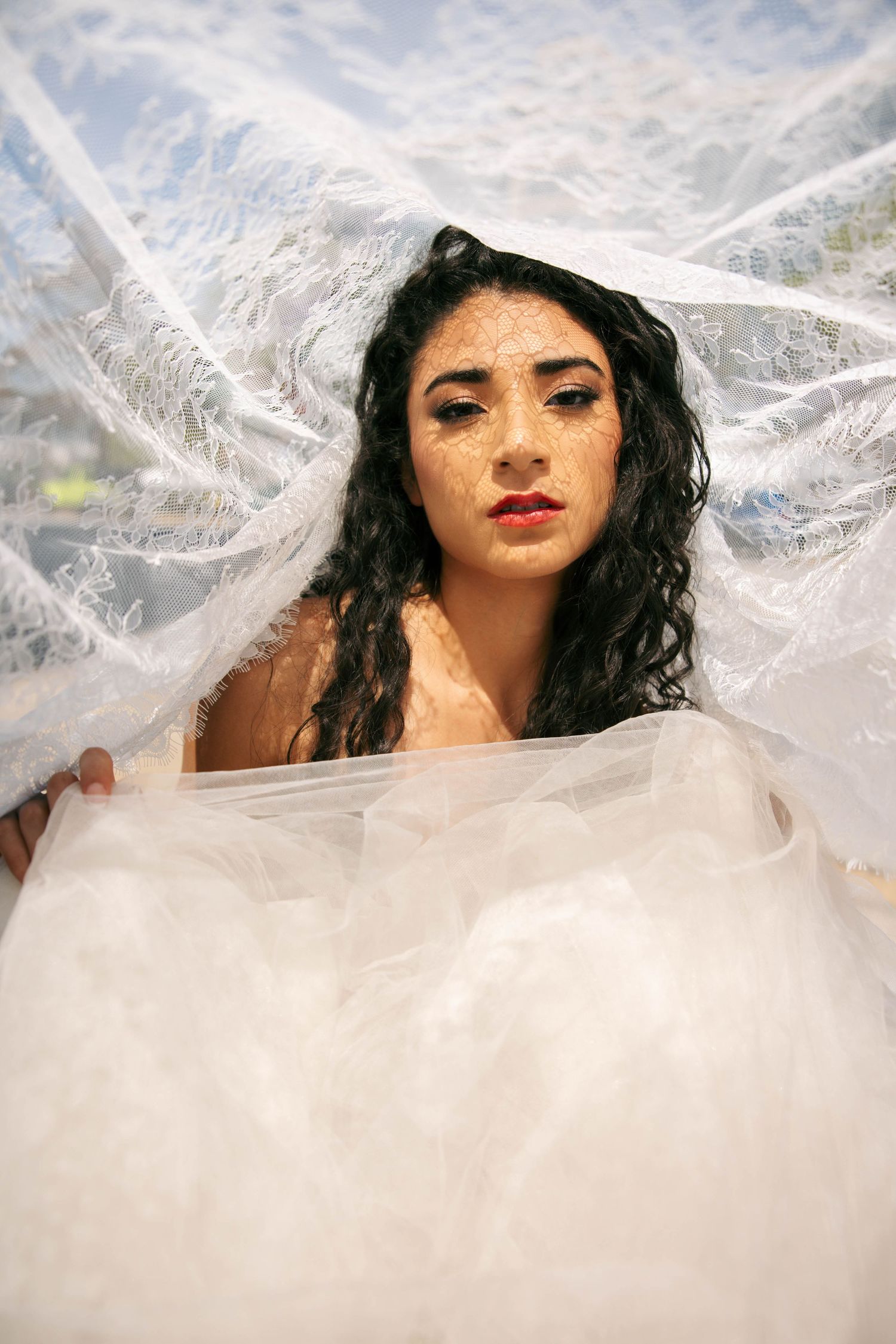 Woman with curly dark hair surrounded by translucent white fabric in an artistic portrait photo.