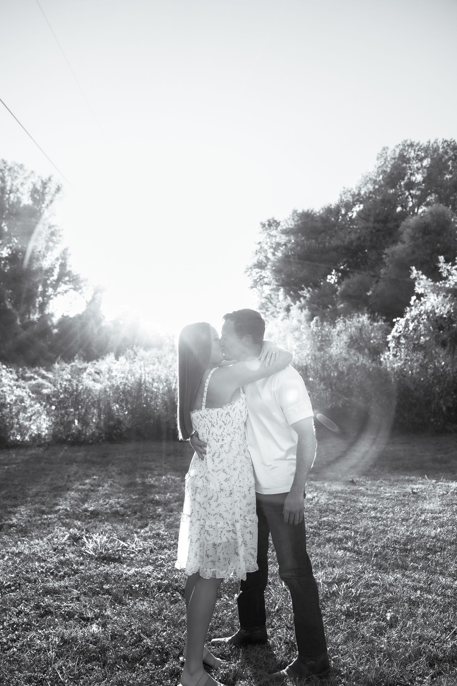 Couple embraces in sunlit field during black and white photoshoot.