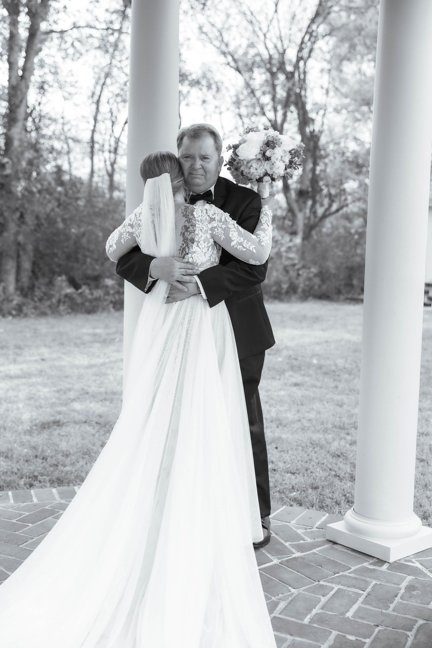 Black and white photo of couple during first look moment between white columns.