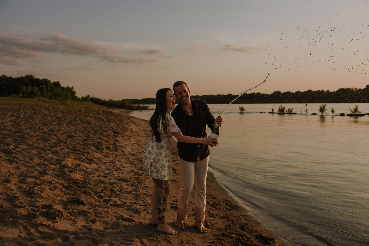 Romantic beach portraits during golden hour with lake and trees in background.